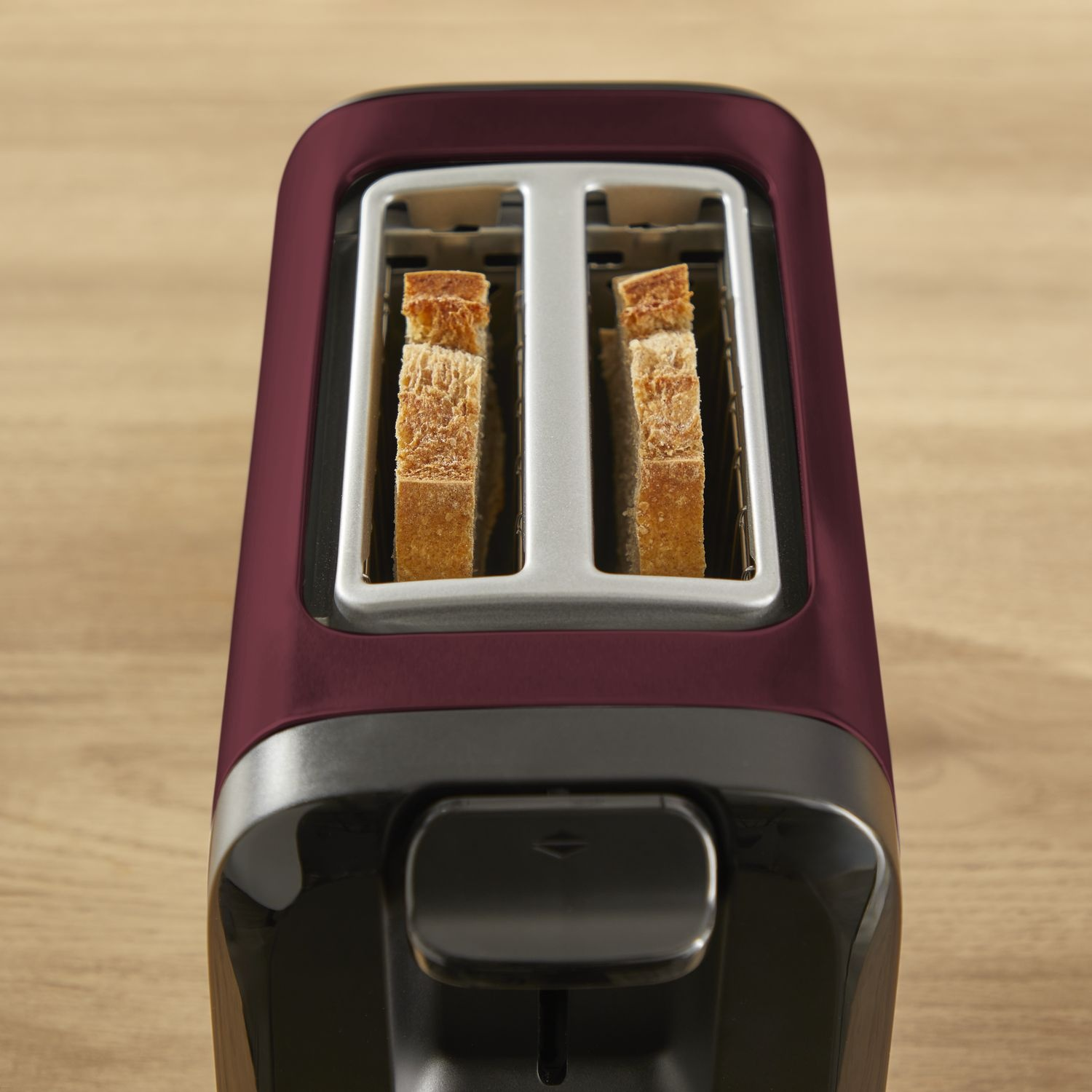 Close-up of a dark red toaster with two slices of toasted bread.