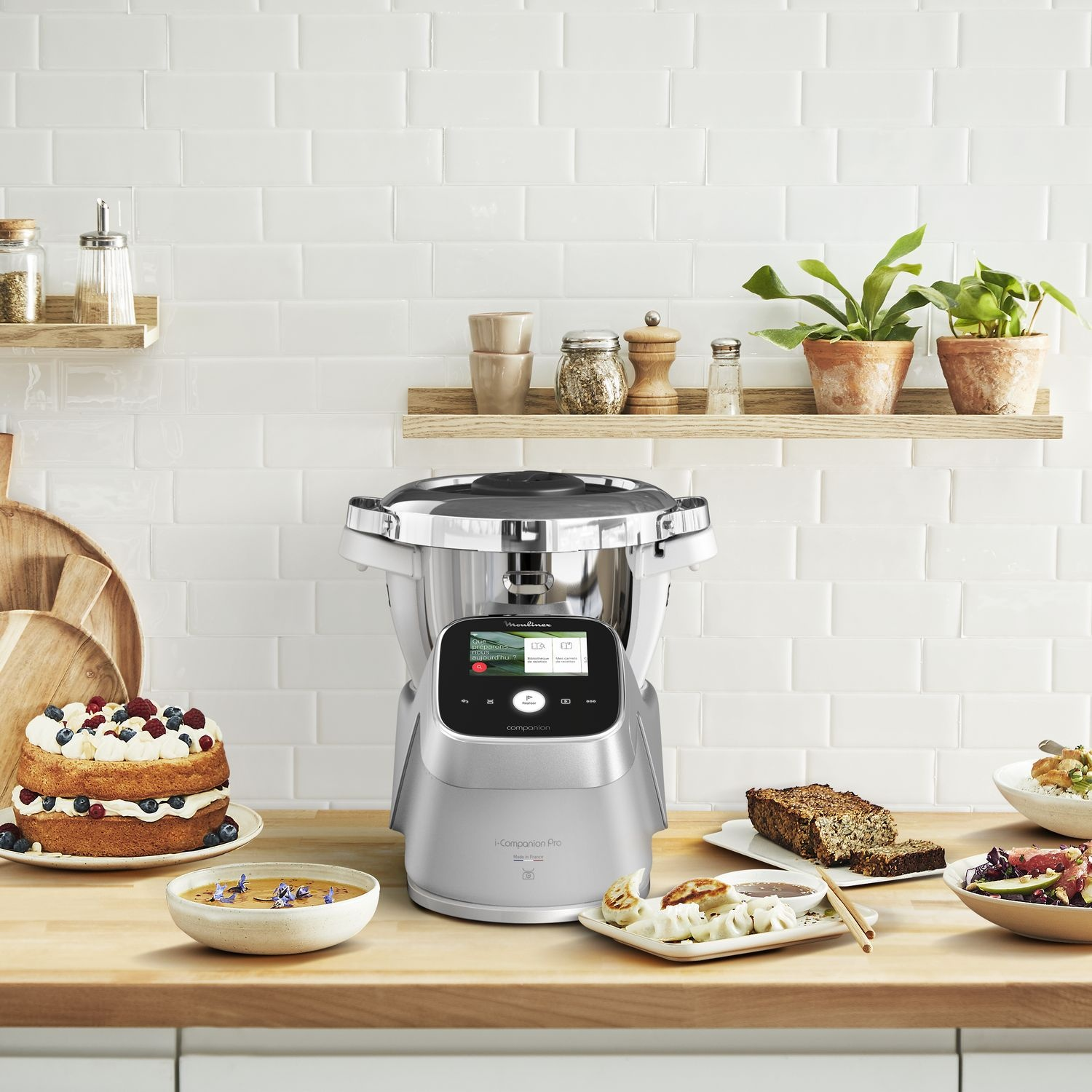 Food processor with food and ingredients around, on a wooden surface, white tiled background.