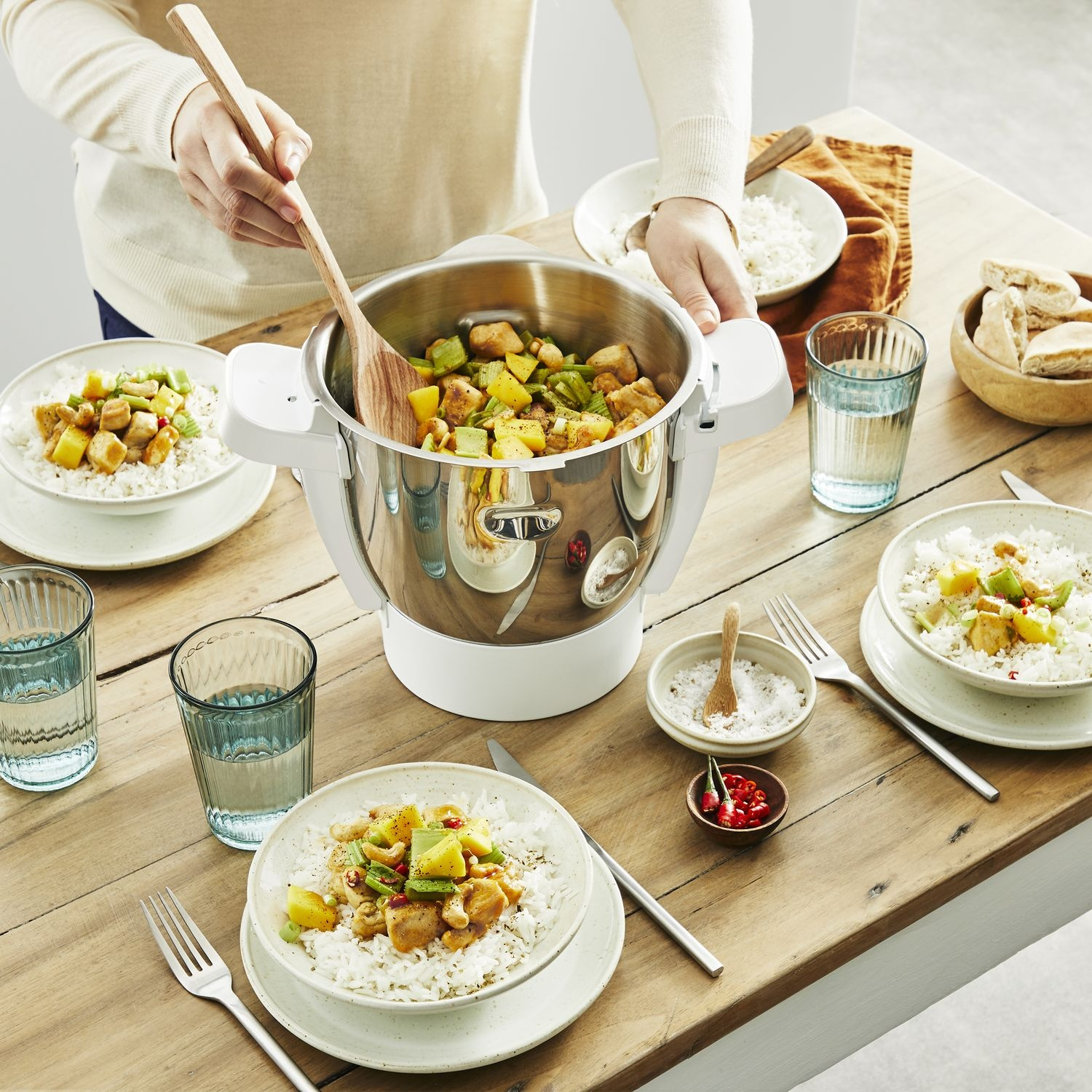 A person is cooking in a pot. There are plates of rice and other food around the pot.