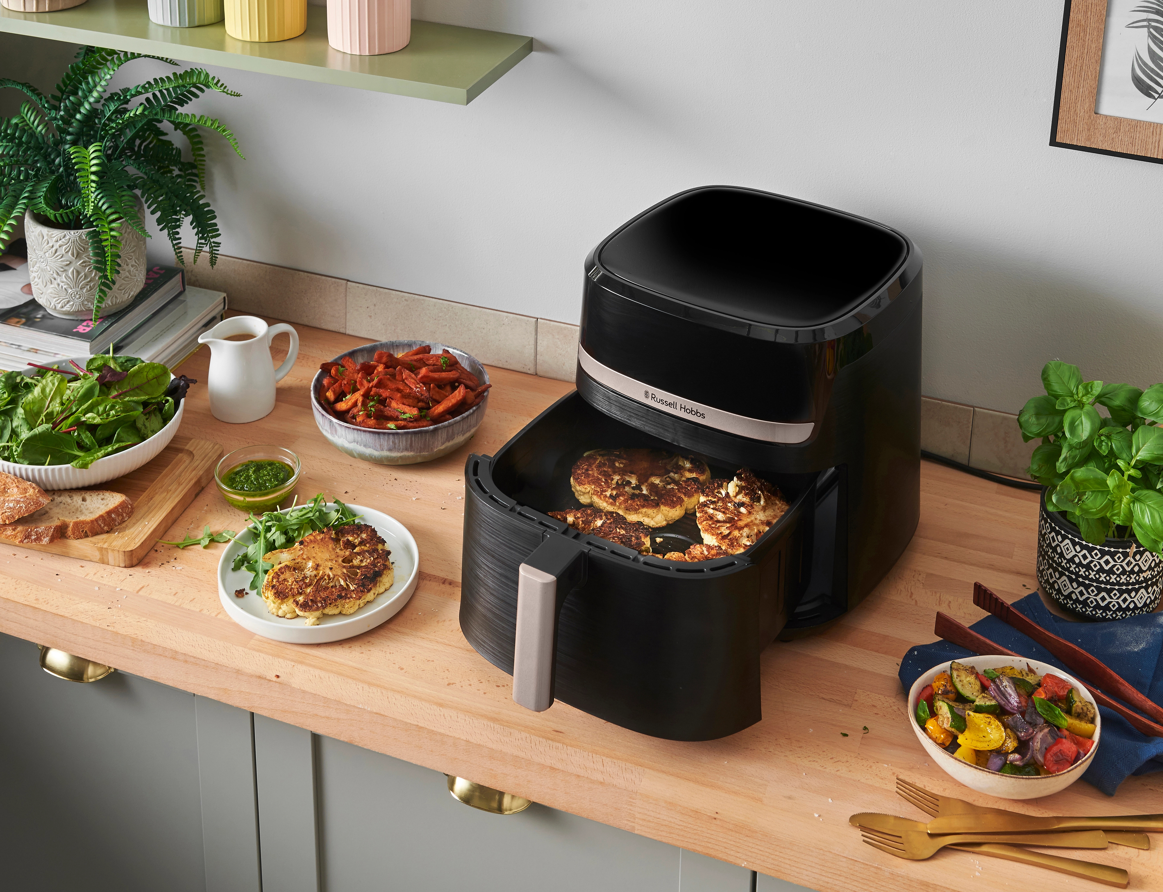 Frytownica beztłuszczowa z jedzeniem w środku i różnymi dodatkami na drewnianym blacie.