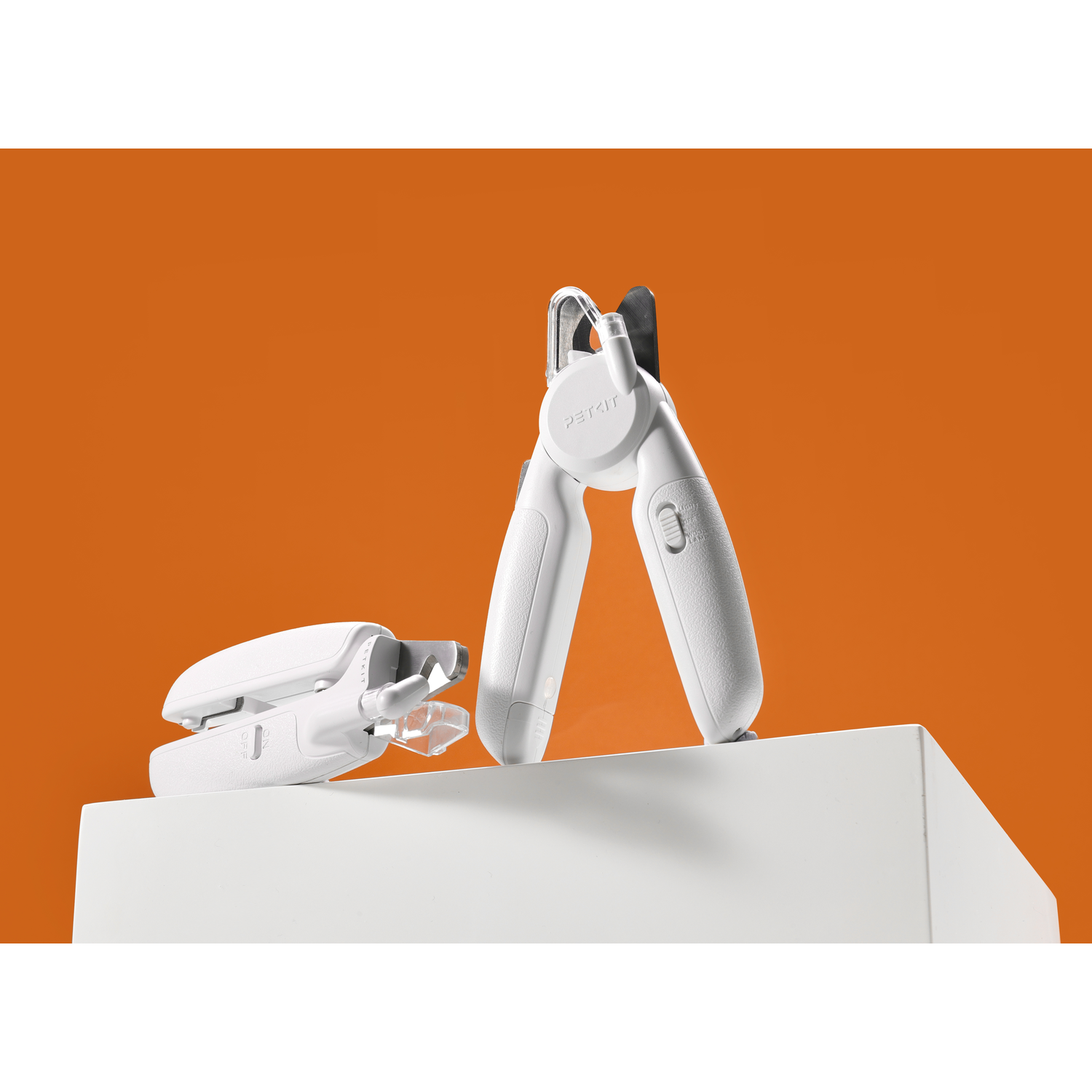 Two white PETKIT nail clippers on a white base against an orange background. One has a light.