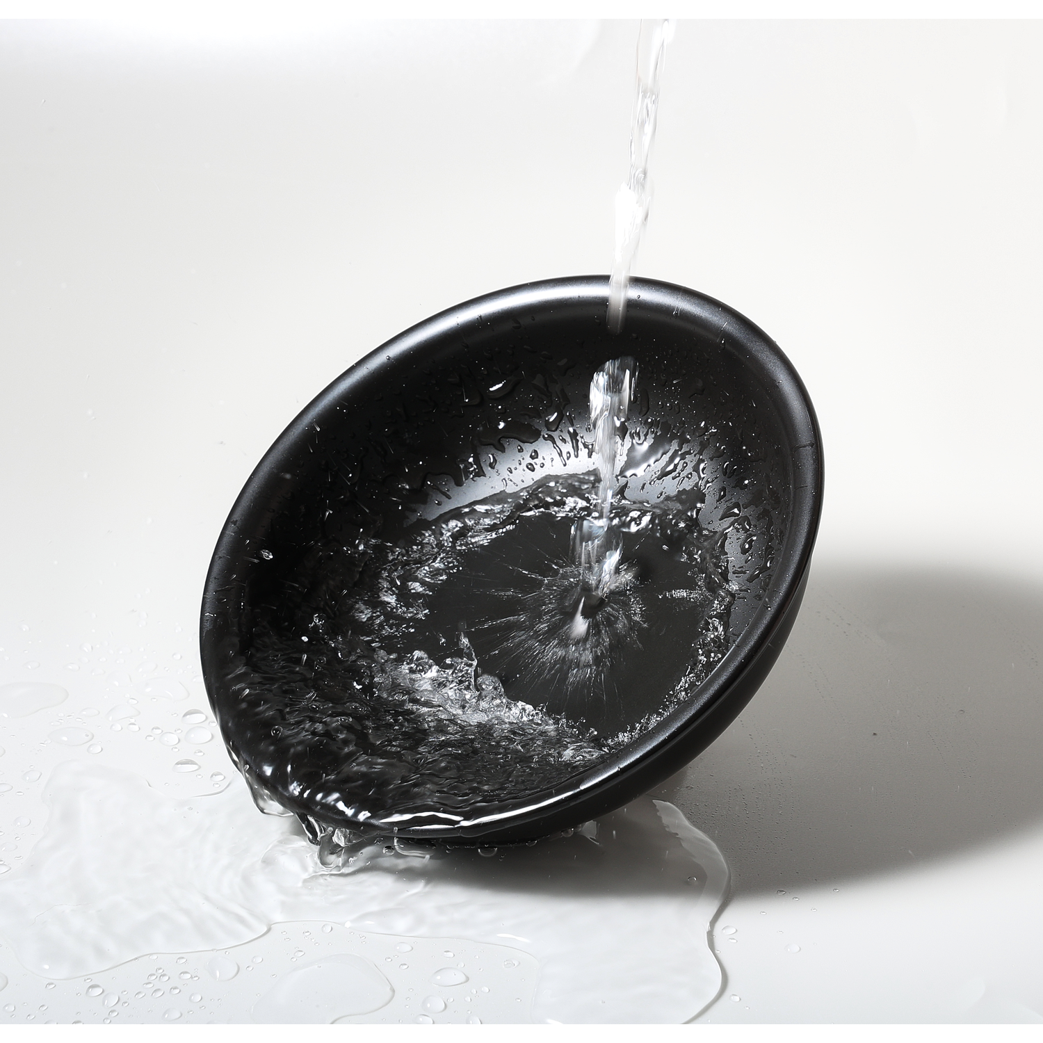 Water pouring into a black oval bowl, creating reflections on a white surface.