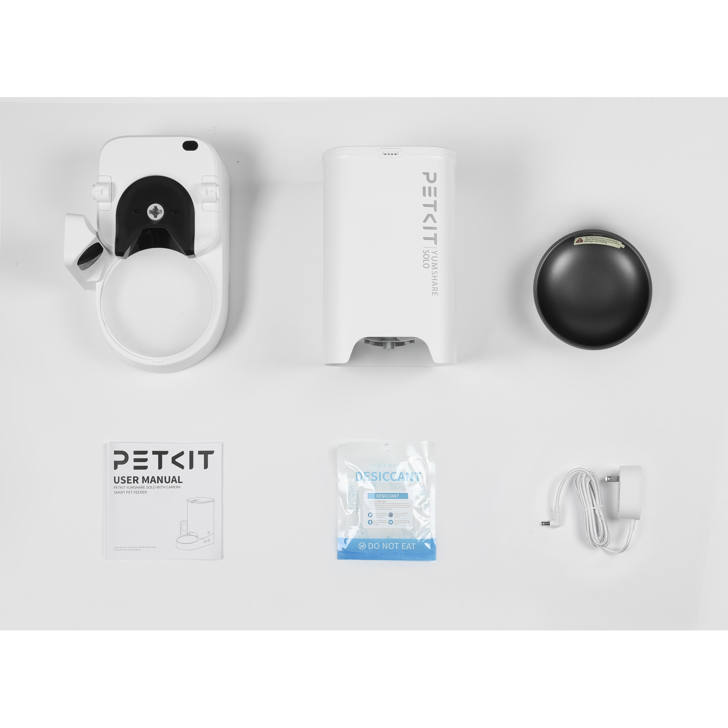 A pet food dispenser and accessories are arranged on a white background, including a bowl and a manual.