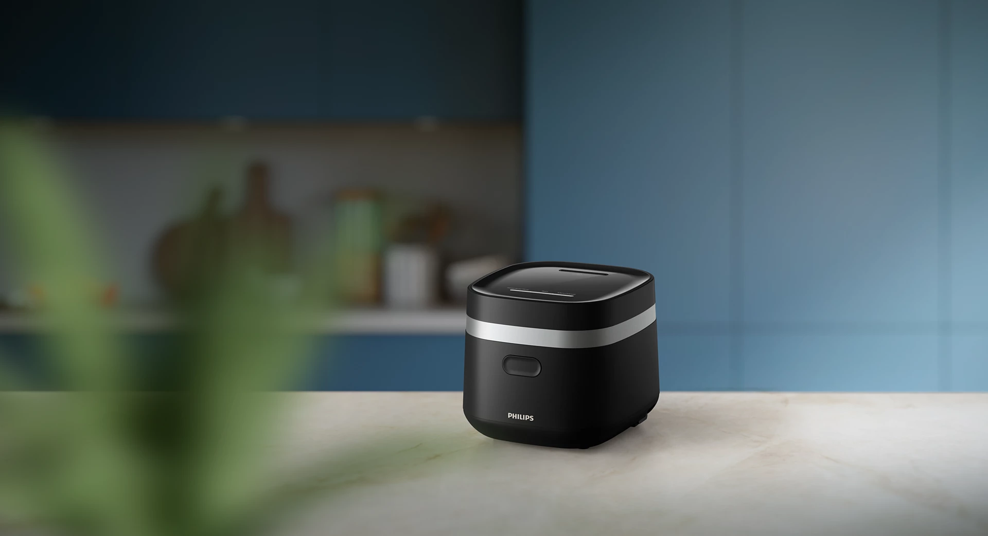Cuociriso Philips nero su un piano di lavoro in marmo. Sfondo sfocato con sfumature blu e verdi.