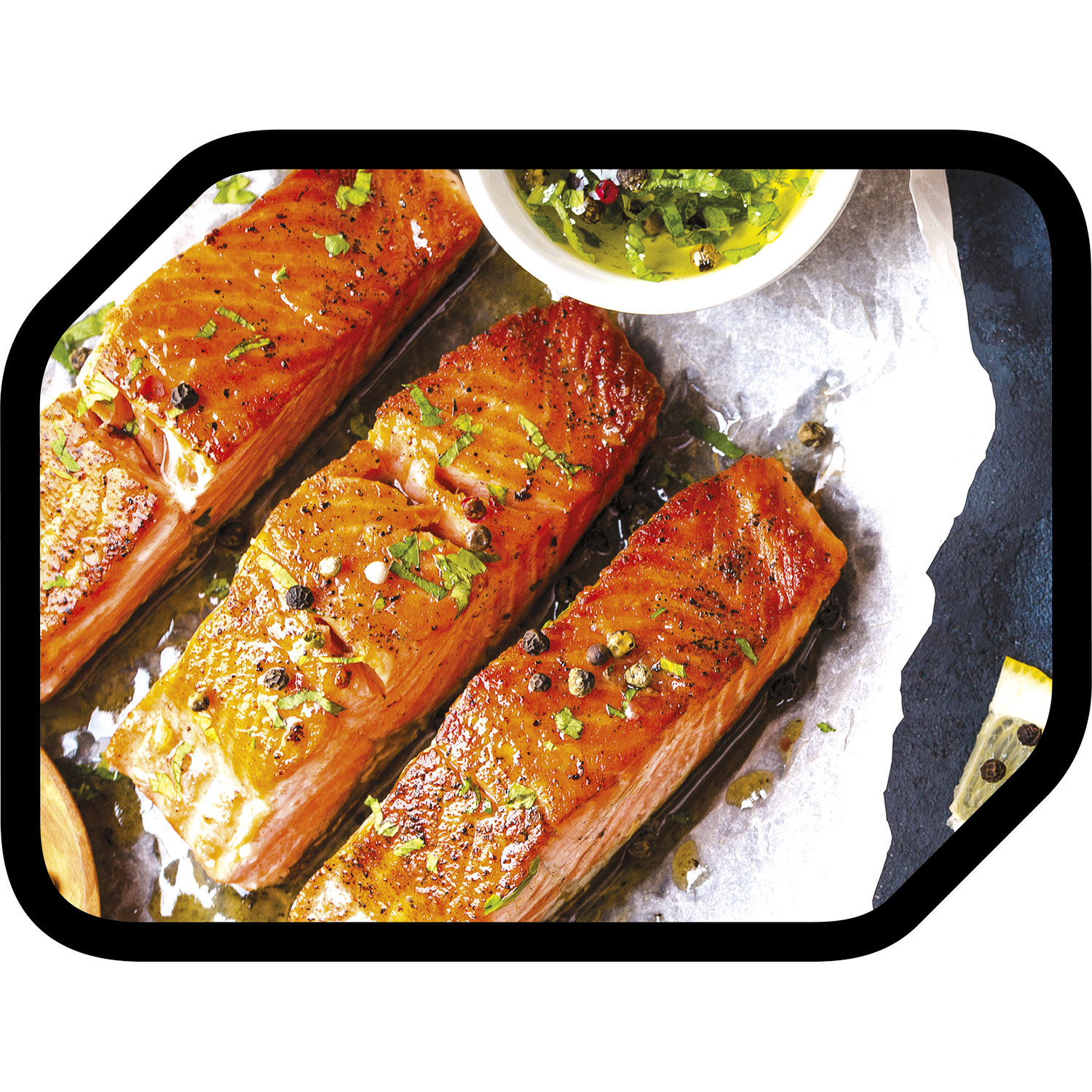 Gegrilde zalmfilets met kruiden, peper en saus op bakpapier. Een klein bakje groene saus is ook zichtbaar.