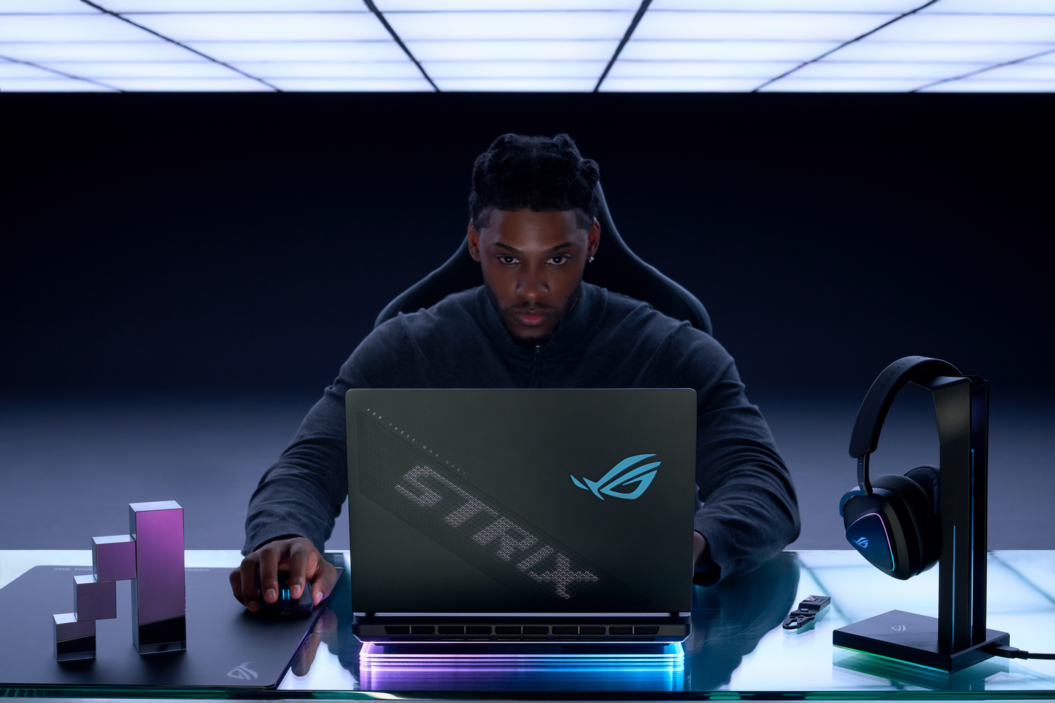 Un hombre usando una laptop con auriculares para juegos y una configuración de escritorio en un ambiente oscuro.