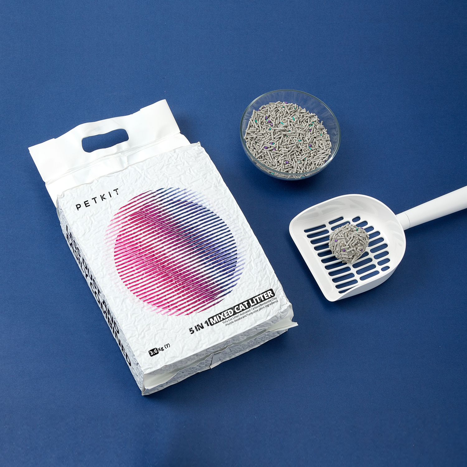 White bag of cat litter, bowl of litter, and a scoop, on a blue surface.