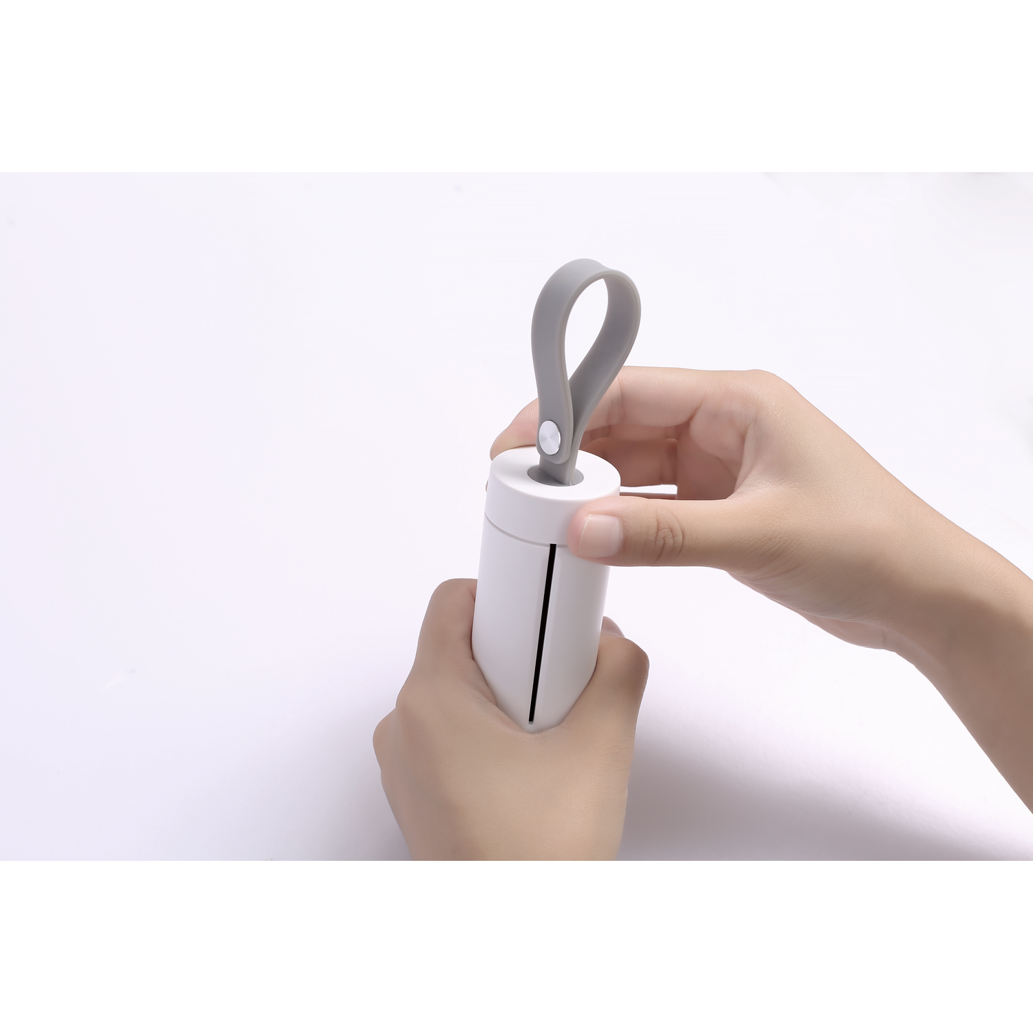 Hands holding a white lint roller with a gray handle. It's being prepared for use.