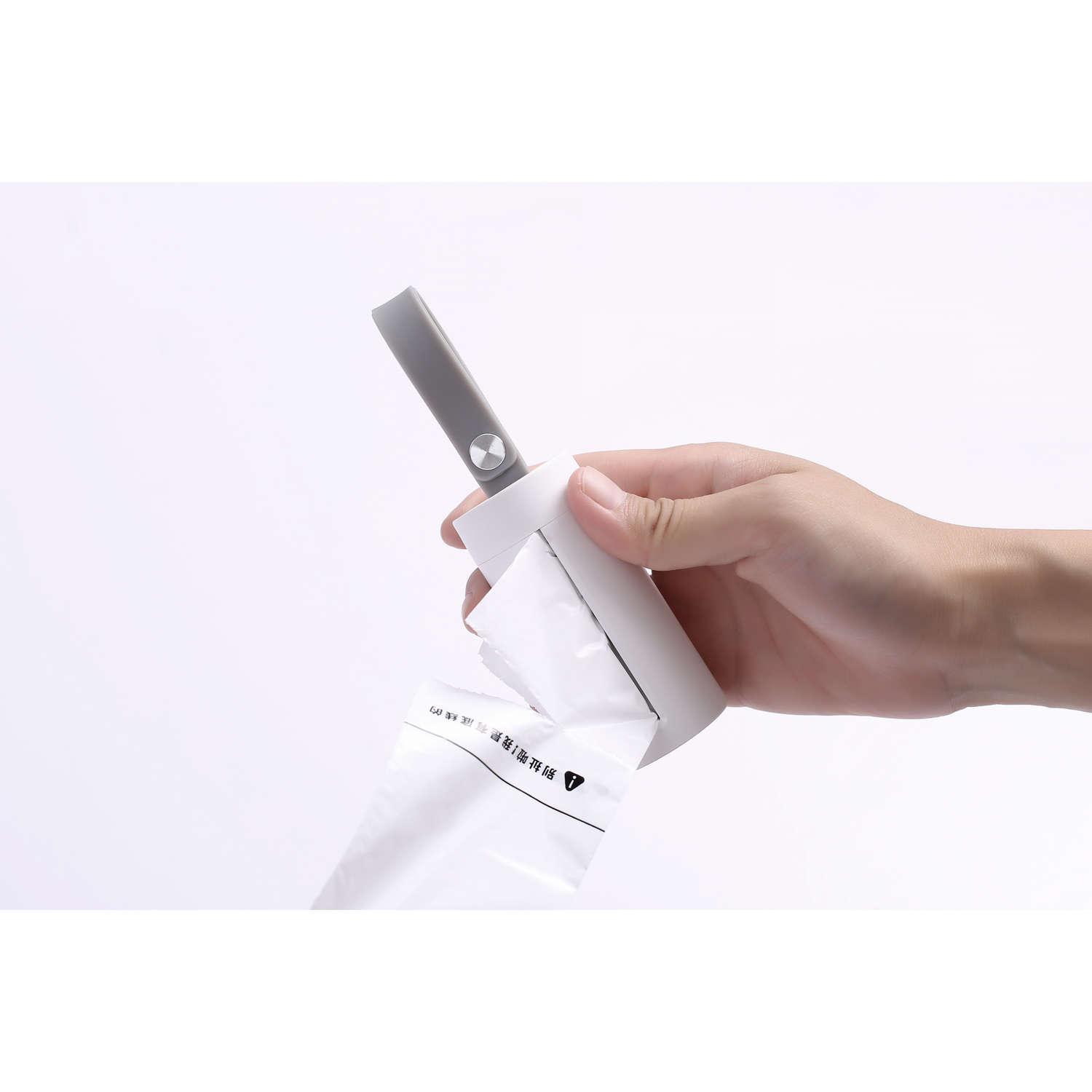 A person's hand holds a white pet waste bag dispenser.