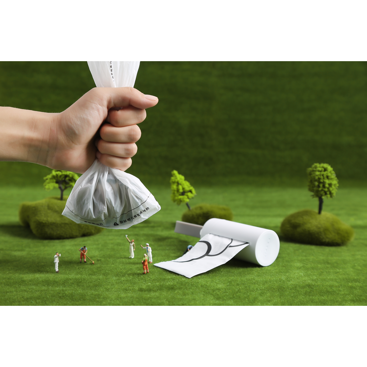 A hand holding a bag of waste while small figurines are cleaning up the ground.