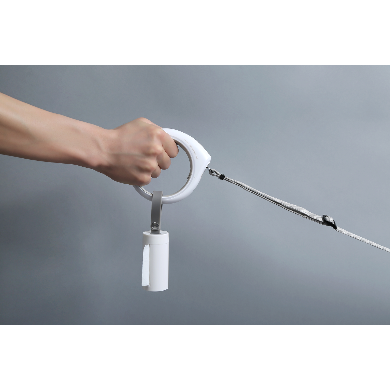 A hand holding a white dog leash with a built-in waste bag dispenser.
