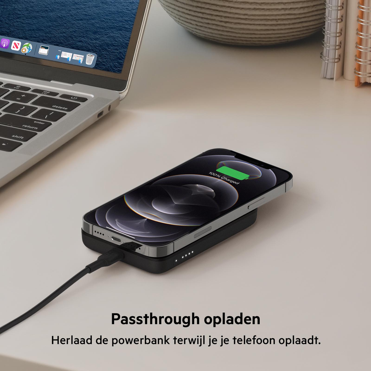 A phone wirelessly charging on a black pad connected to a laptop on a white desk.