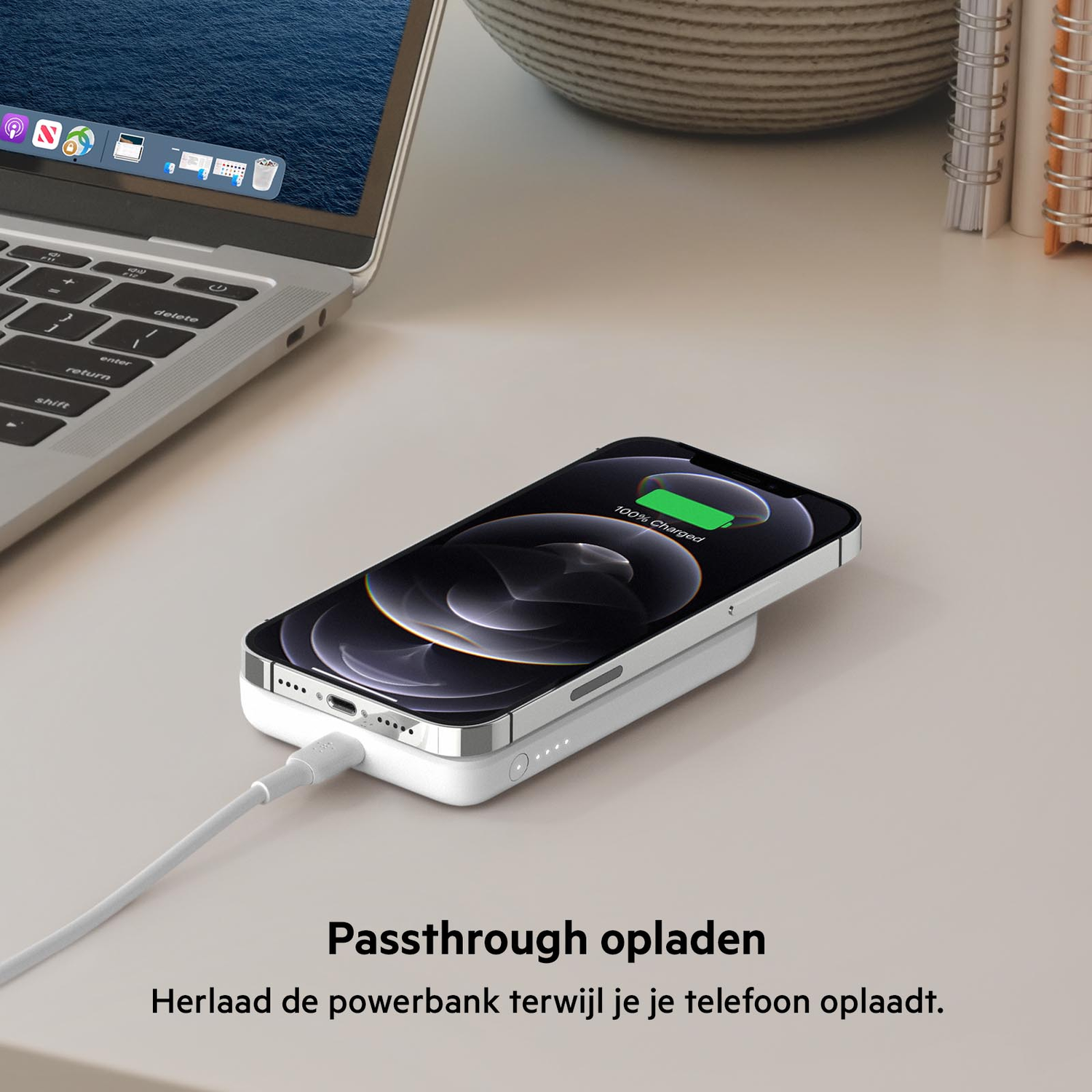 A smartphone charging wirelessly on a white pad connected to a laptop with a white cable.