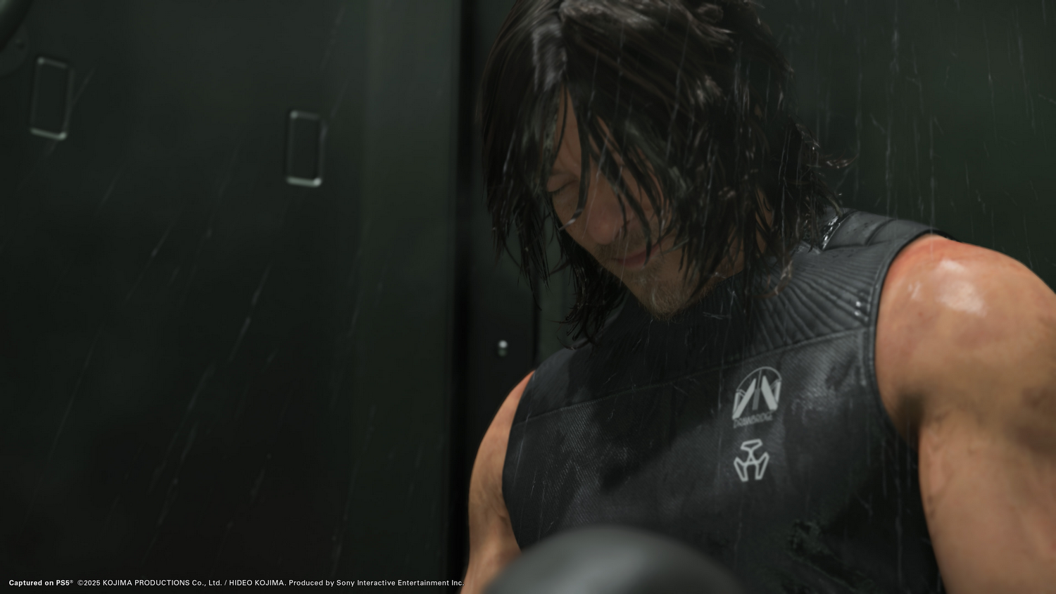 Hombre con cabello oscuro, camiseta sin mangas negra, mirando hacia abajo con expresión dolorida, lluvia cayendo.