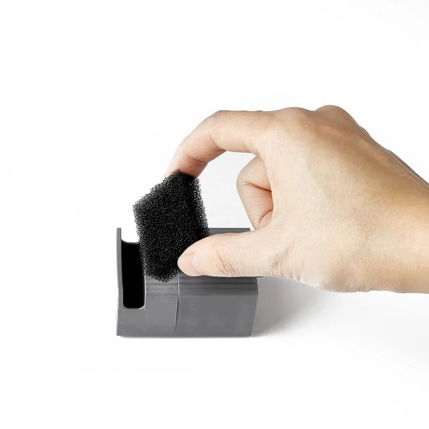 A hand holding a black sponge, putting it into a gray container.