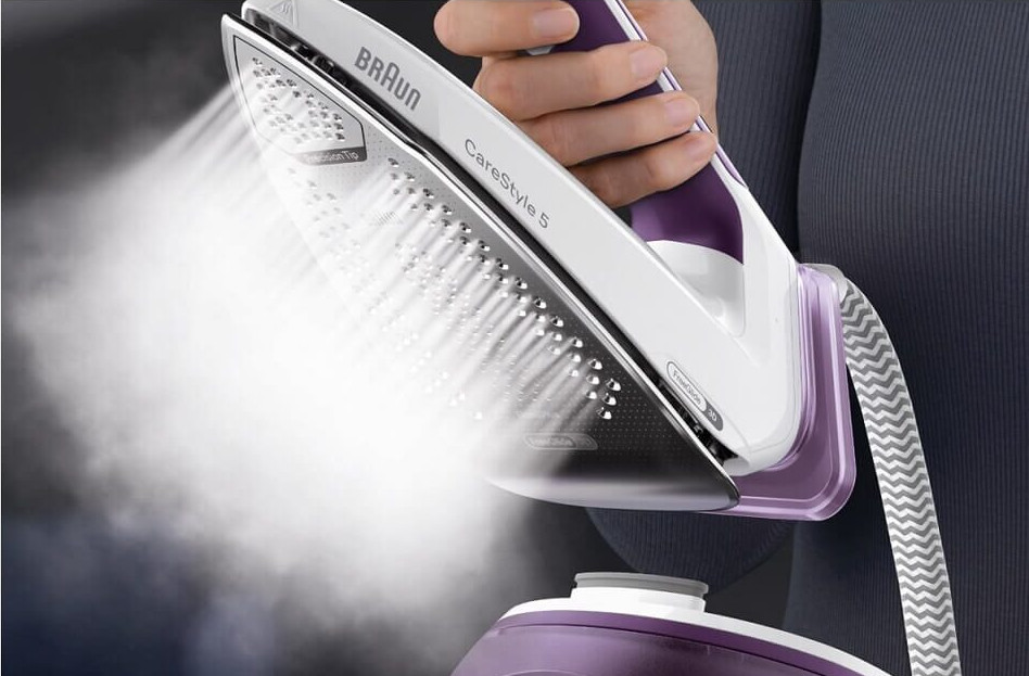 Osoba prasująca szarą koszulę biało-fioletowym żelazkiem parowym.