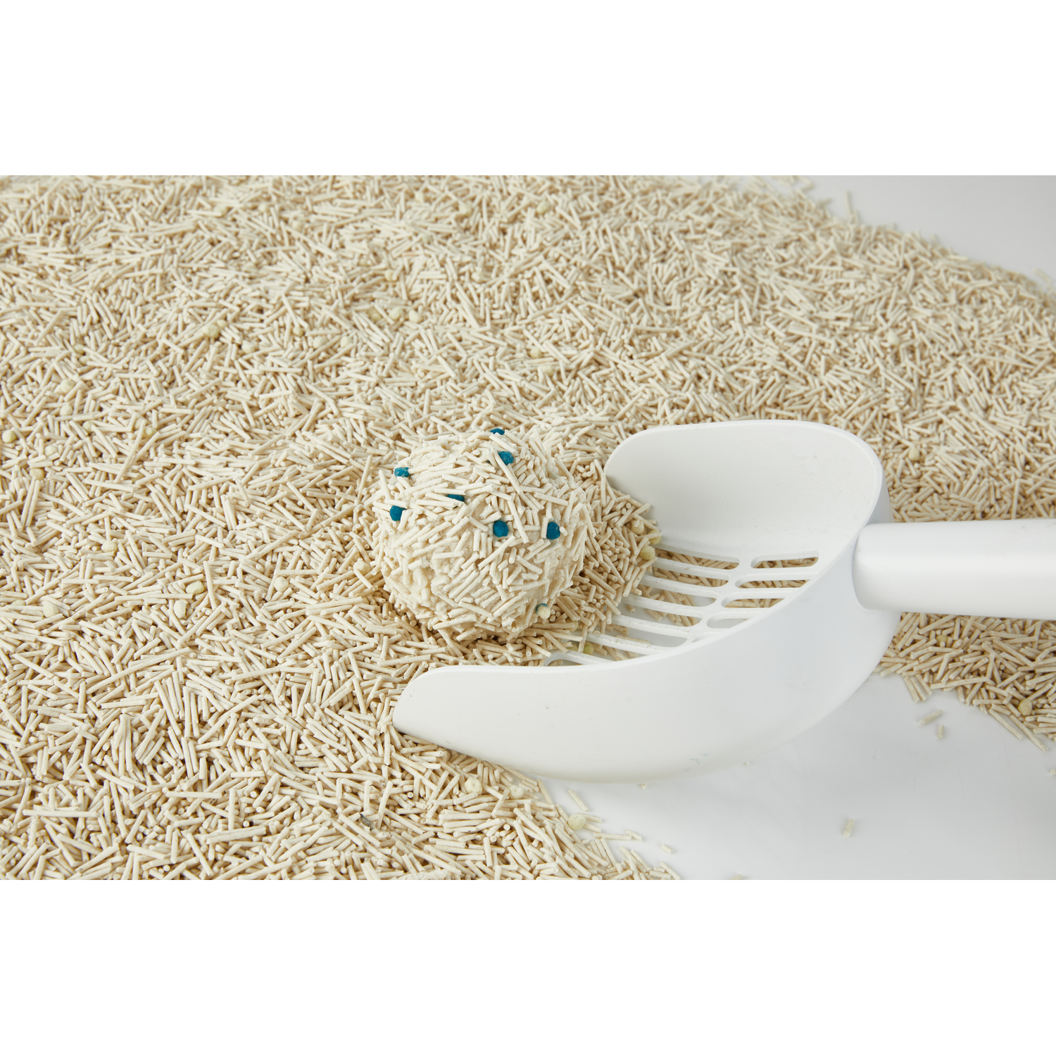Een witte kattenbakschep schept een bal kattenbakvulling. De vulling is lichtbruin van kleur.