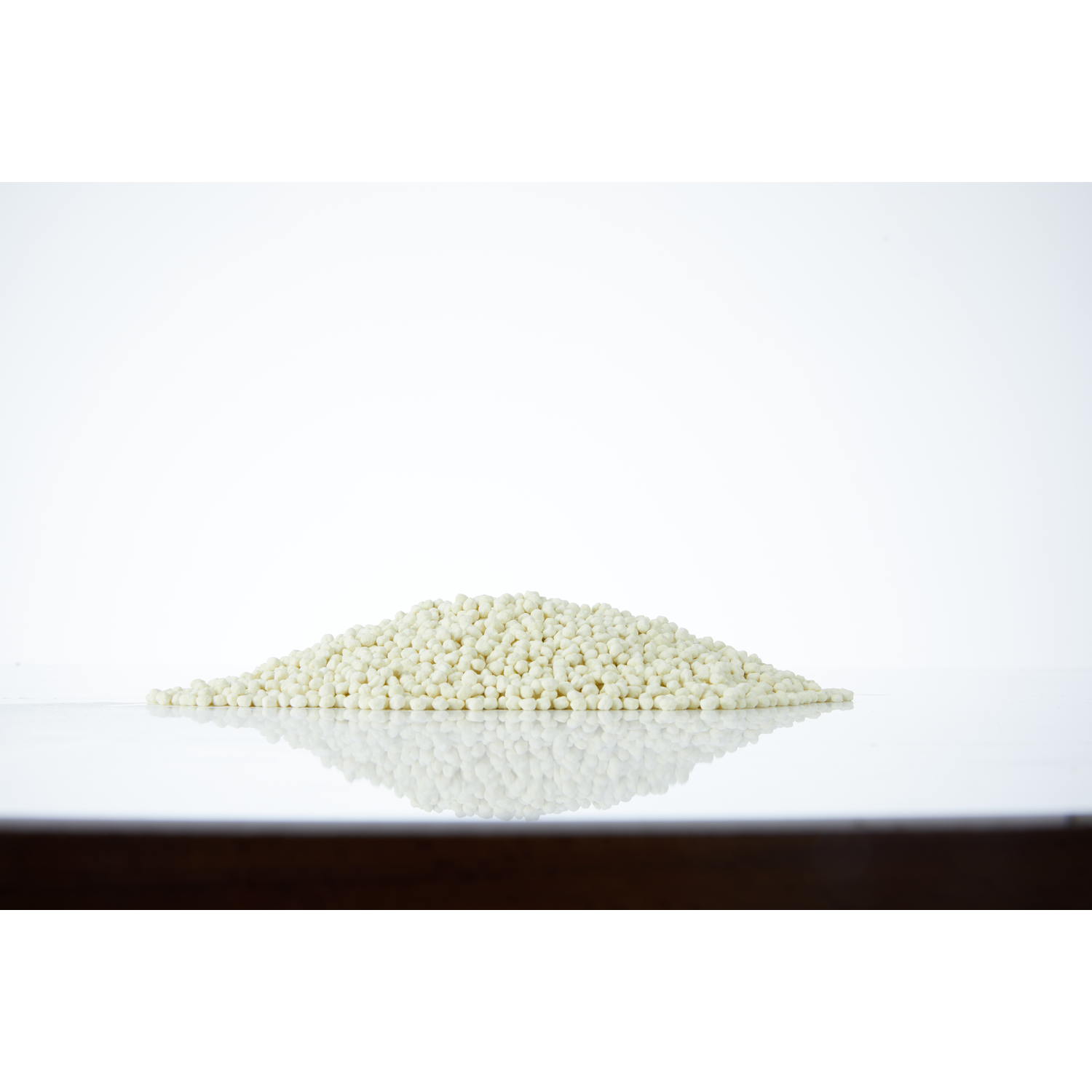 Een stapel witte, bolvormige pellets op een reflecterend oppervlak, witte achtergrond.