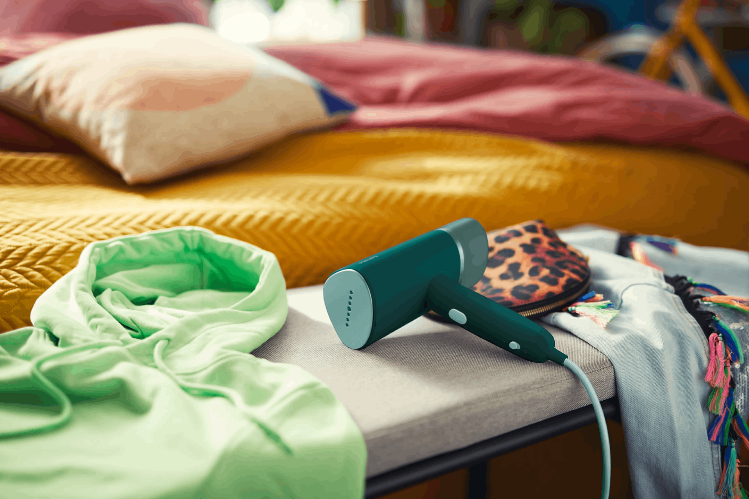 Una sudadera con capucha verde en una cama con un vaporizador de ropa.