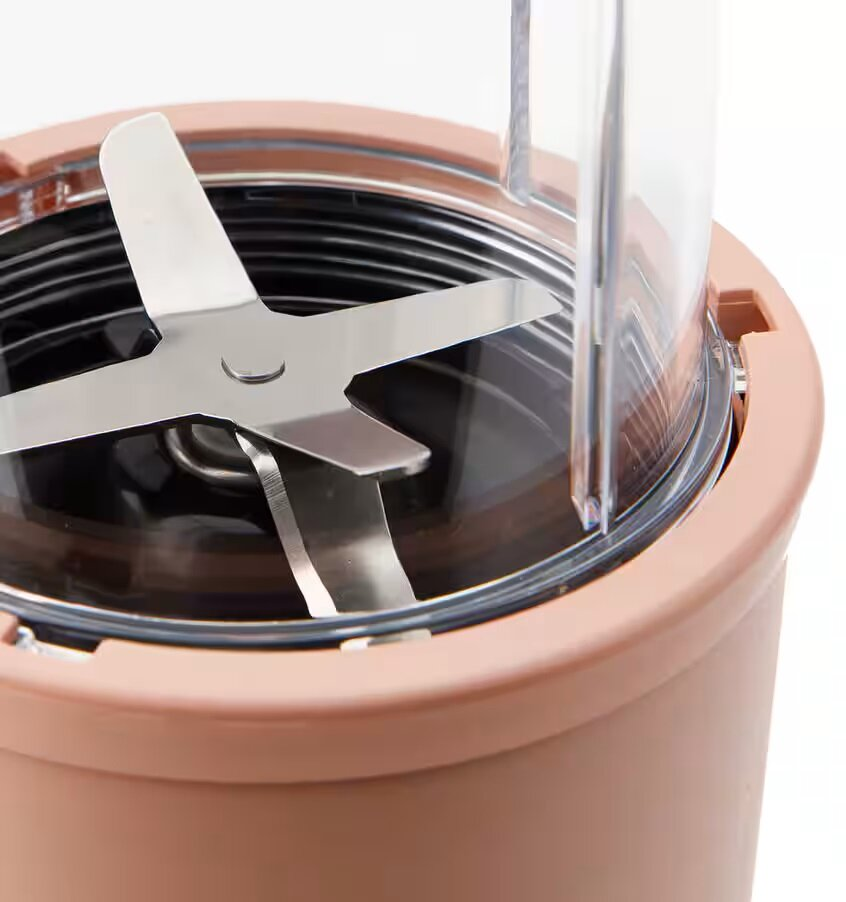 Zespół ostrzy blendera wewnątrz beżowego pojemnika, z białym tłem.