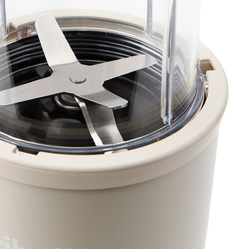 Zbliżenie blendera. Ostrze jest srebrne, pojemnik przezroczysty, a podstawa beżowa.