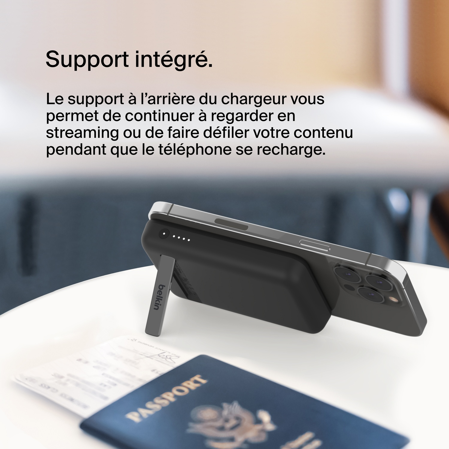 Un téléphone repose sur un chargeur noir avec un support. Un passeport et un papier sont sur la table.
