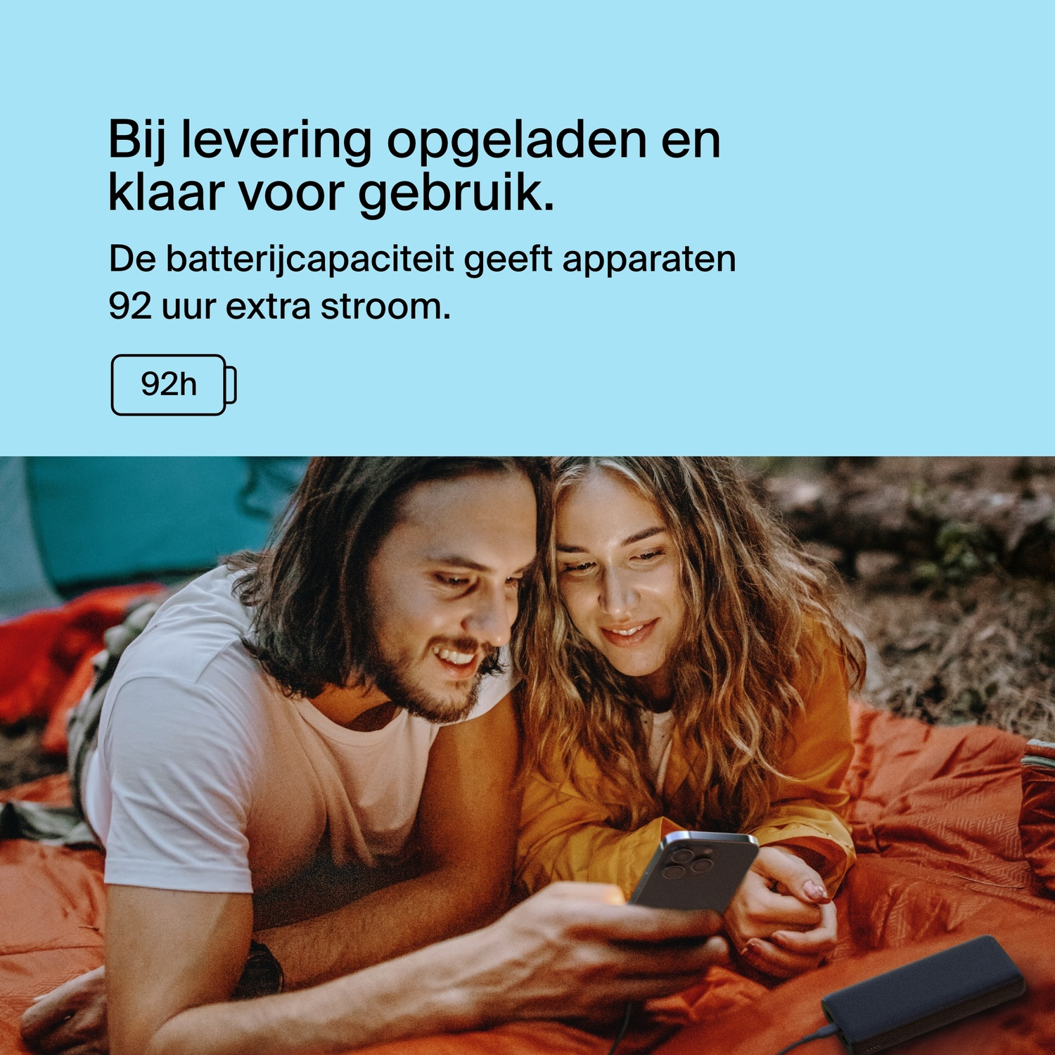 Two people looking at a phone connected to a power bank, set up with camping gear.