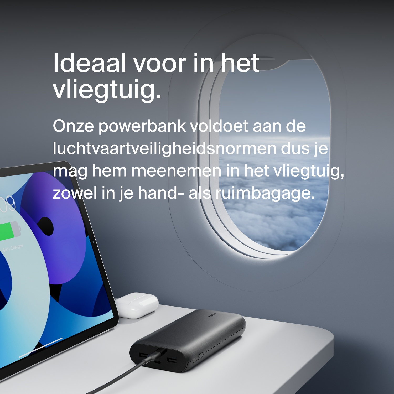A black power bank and a tablet on a table, with a window showing a sky view.