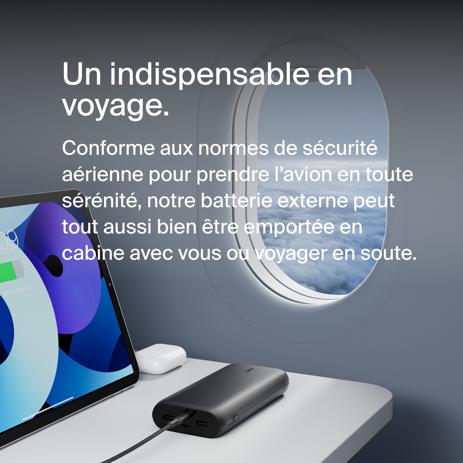 Texte sur une fenêtre d'avion, avec une tablette et des écouteurs sur la table, batterie externe noire.