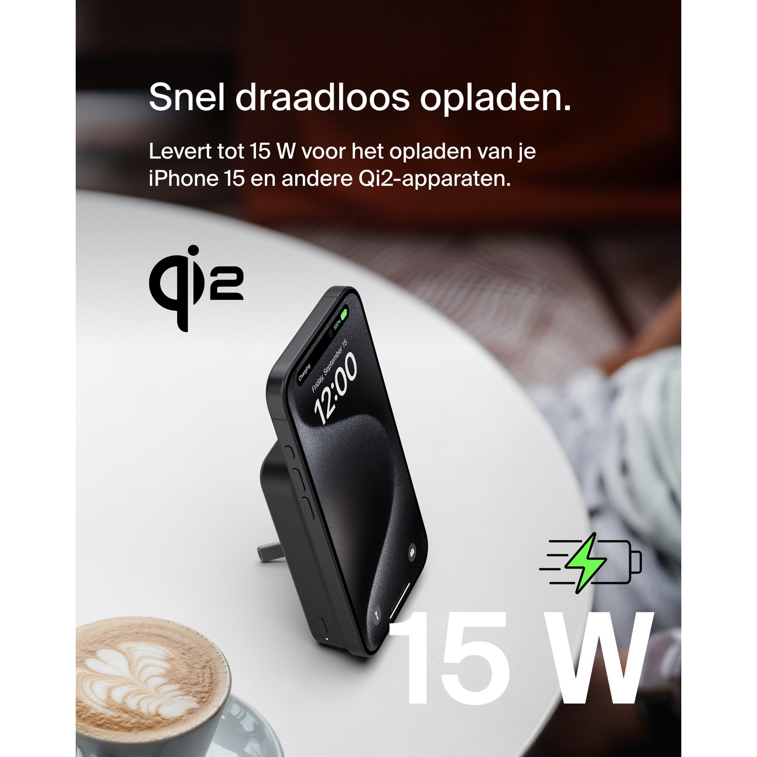 Een draadloze oplader met een zwarte telefoon erop. De oplader staat op een witte tafel, met koffie.