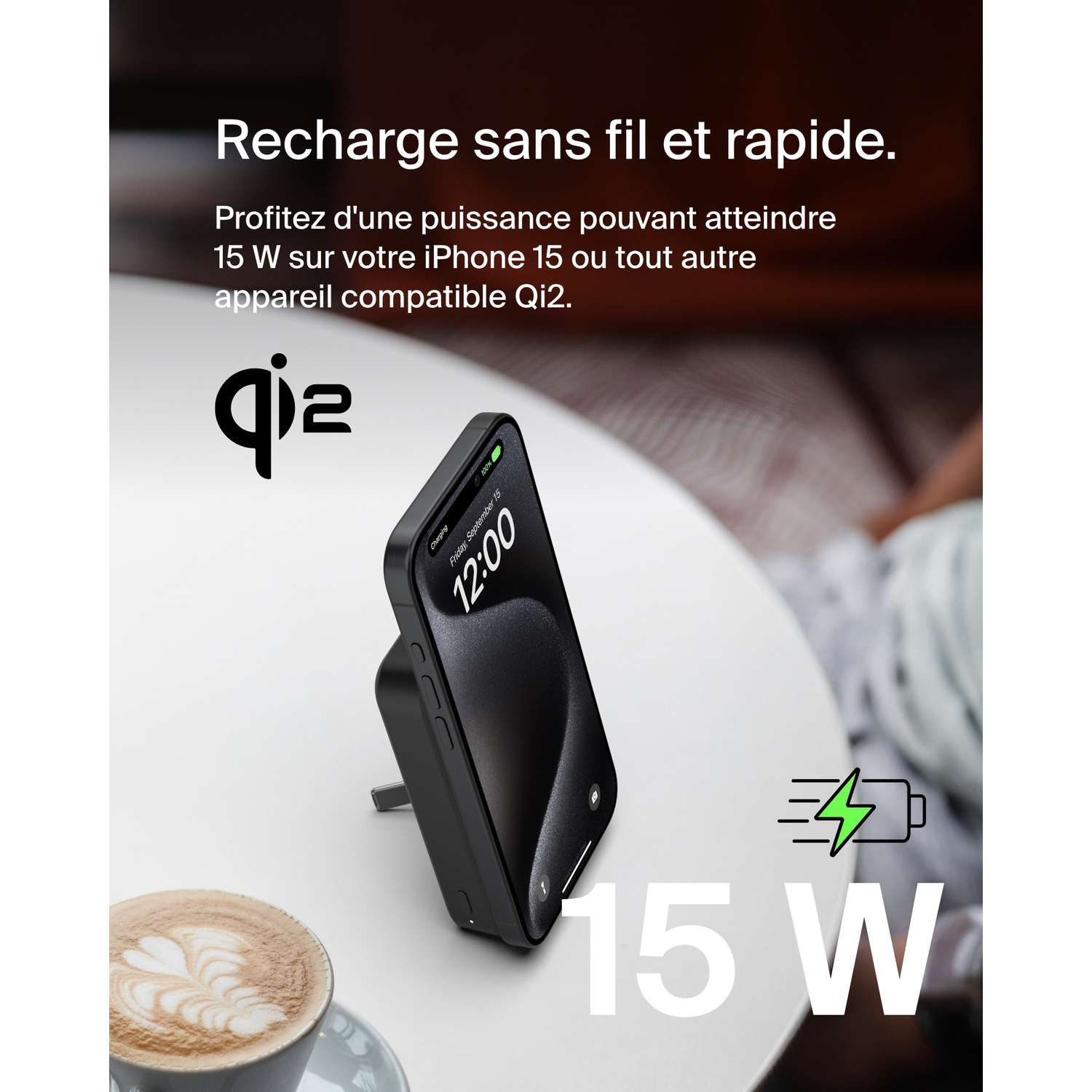 Téléphone en charge sur un socle de charge sans fil. L'écran affiche 15W, tasse à café sur la table.
