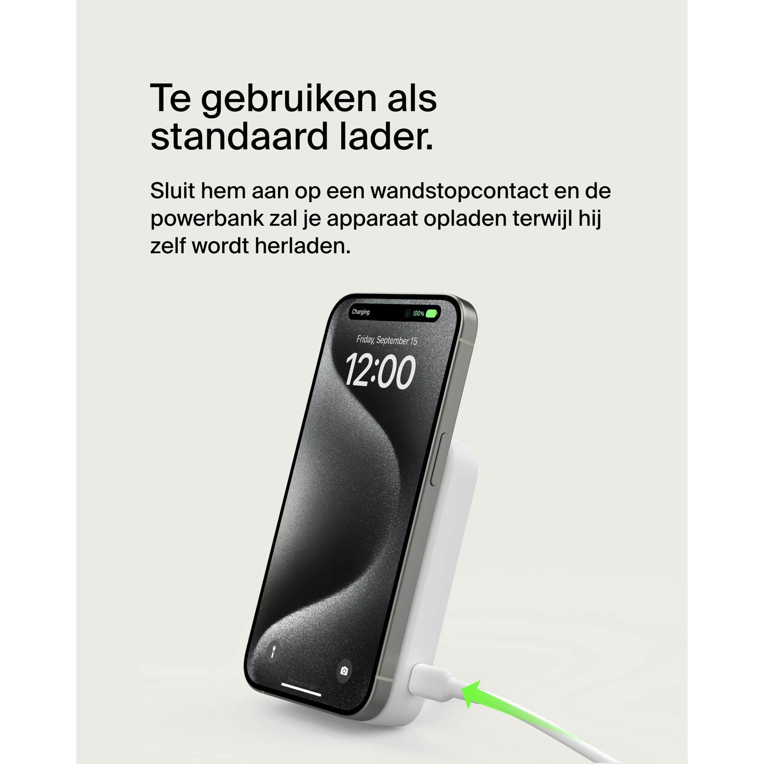A phone charging wirelessly. The phone displays the time 12:00. A white charger is connected to a wall.