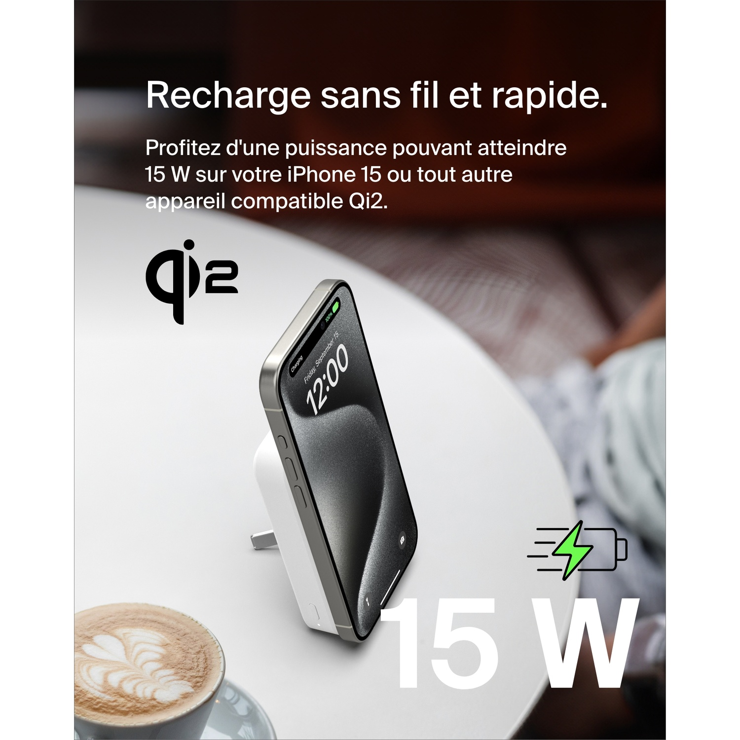 Un téléphone se charge sans fil. Une tasse de café est sur la table. Le téléphone affiche 12h00.