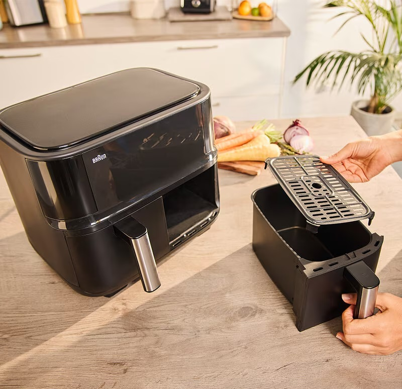 Frytkownica beztłuszczowa z wyjętym koszem, pokazująca osobę trzymającą ruszt.