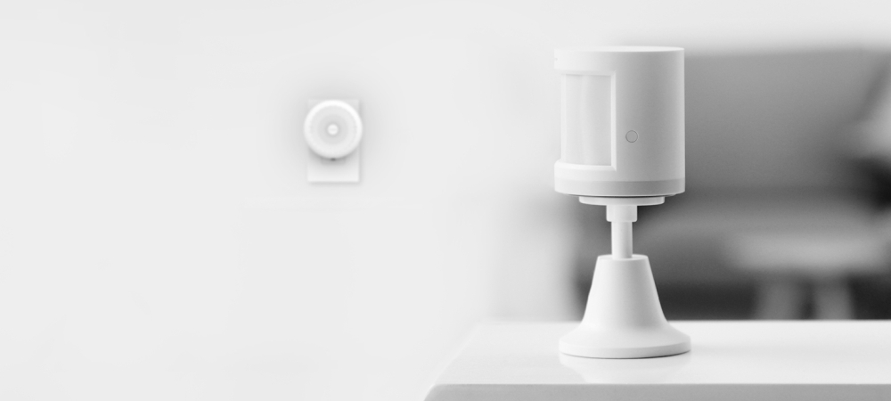 Biały czujnik ruchu na stole, drugi na ścianie. Tło jest rozmyte.