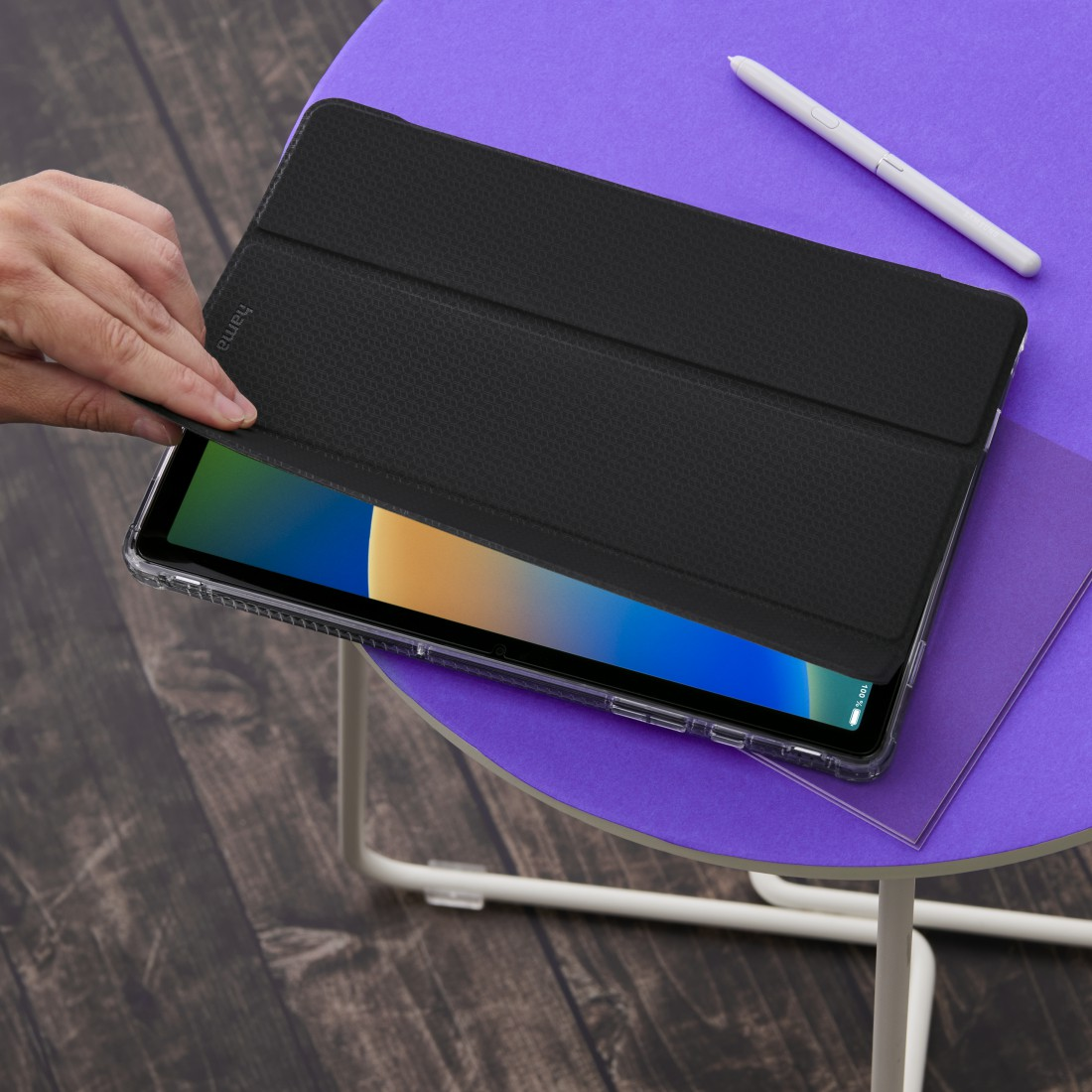 Schwarze Tablethülle auf einem lila Tisch. Ein Stift und ein Tablet sind ebenfalls sichtbar.