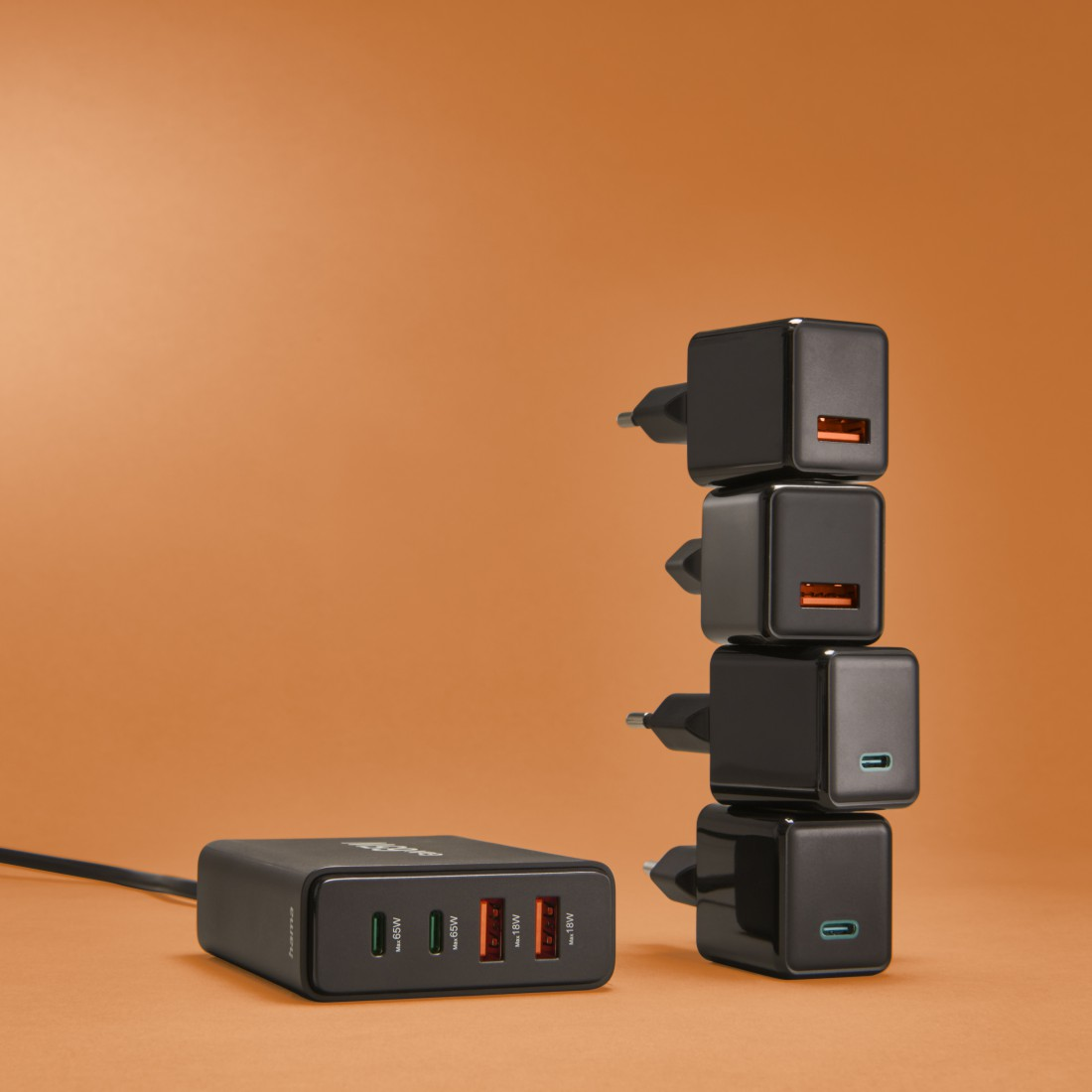 Ein Turm aus schwarzen Ladegerät-Würfeln mit orangefarbenen und blauen USB-Anschlüssen auf orangefarbenem Hintergrund.