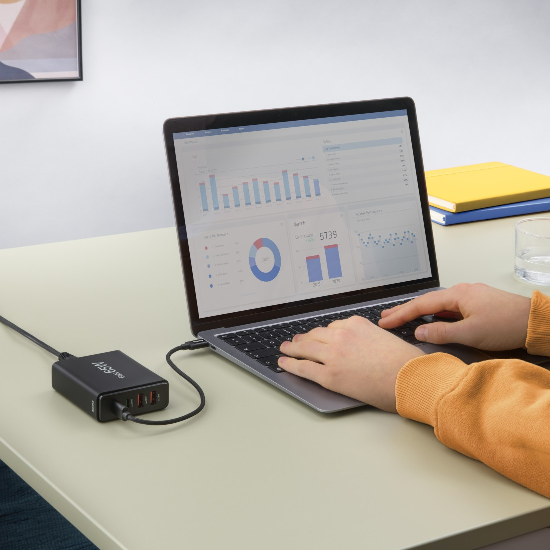 Person tippt auf Laptop, verbunden mit schwarzem Netzteil mit USB-Anschlüssen.