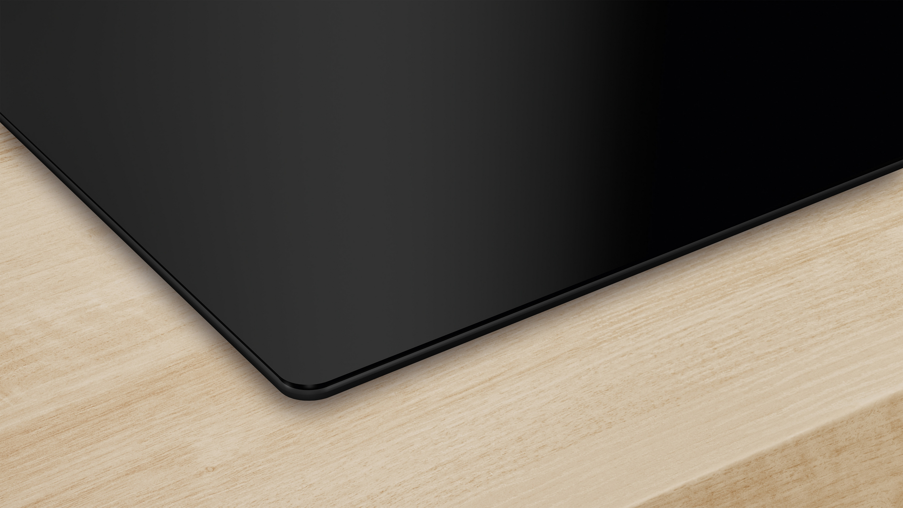 Zbliżenie czarnej, eleganckiej, prostokątnej płyty grzejnej na jasnej drewnianej powierzchni.