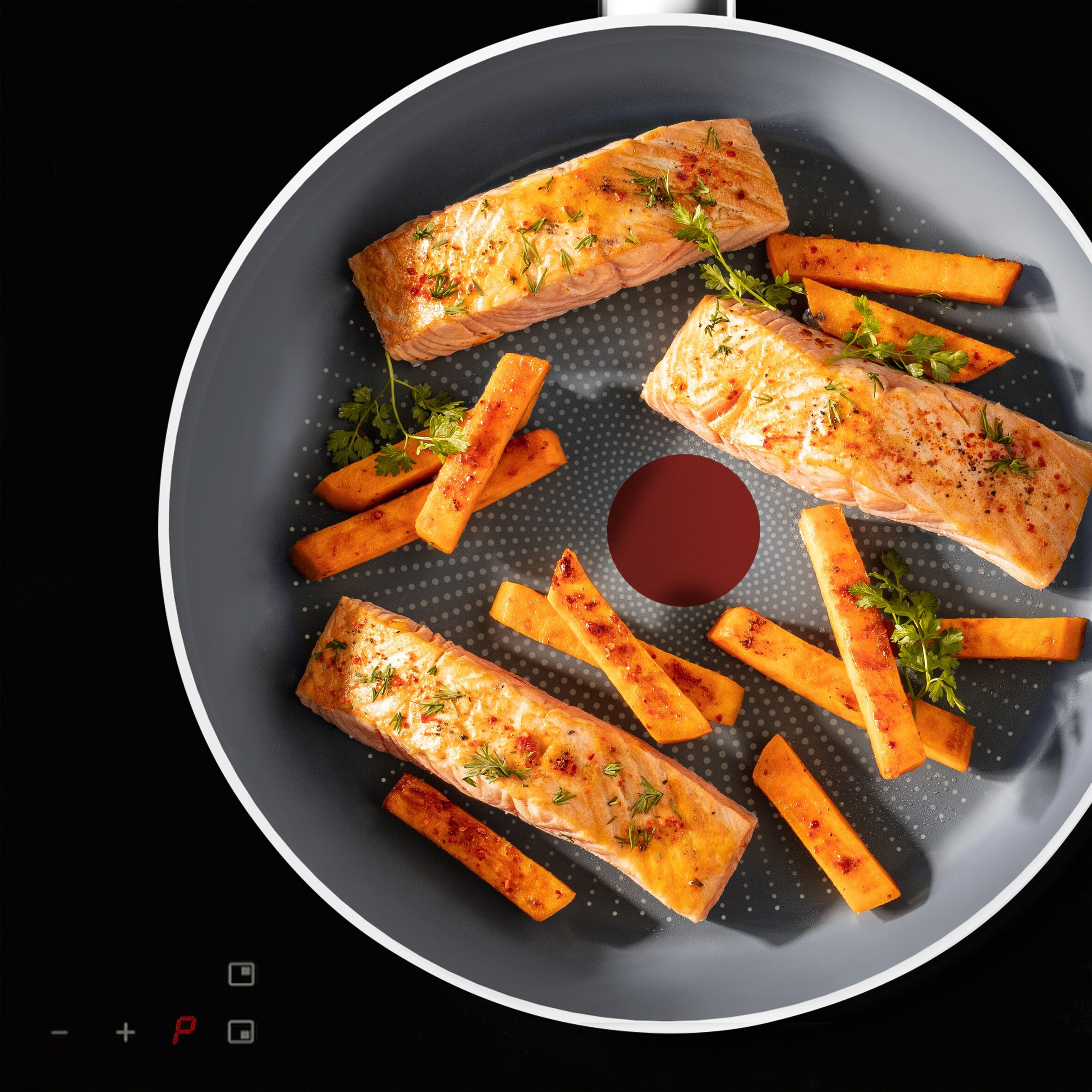 Filety z łososia i frytki z batatów na patelni na czarnej płycie indukcyjnej.