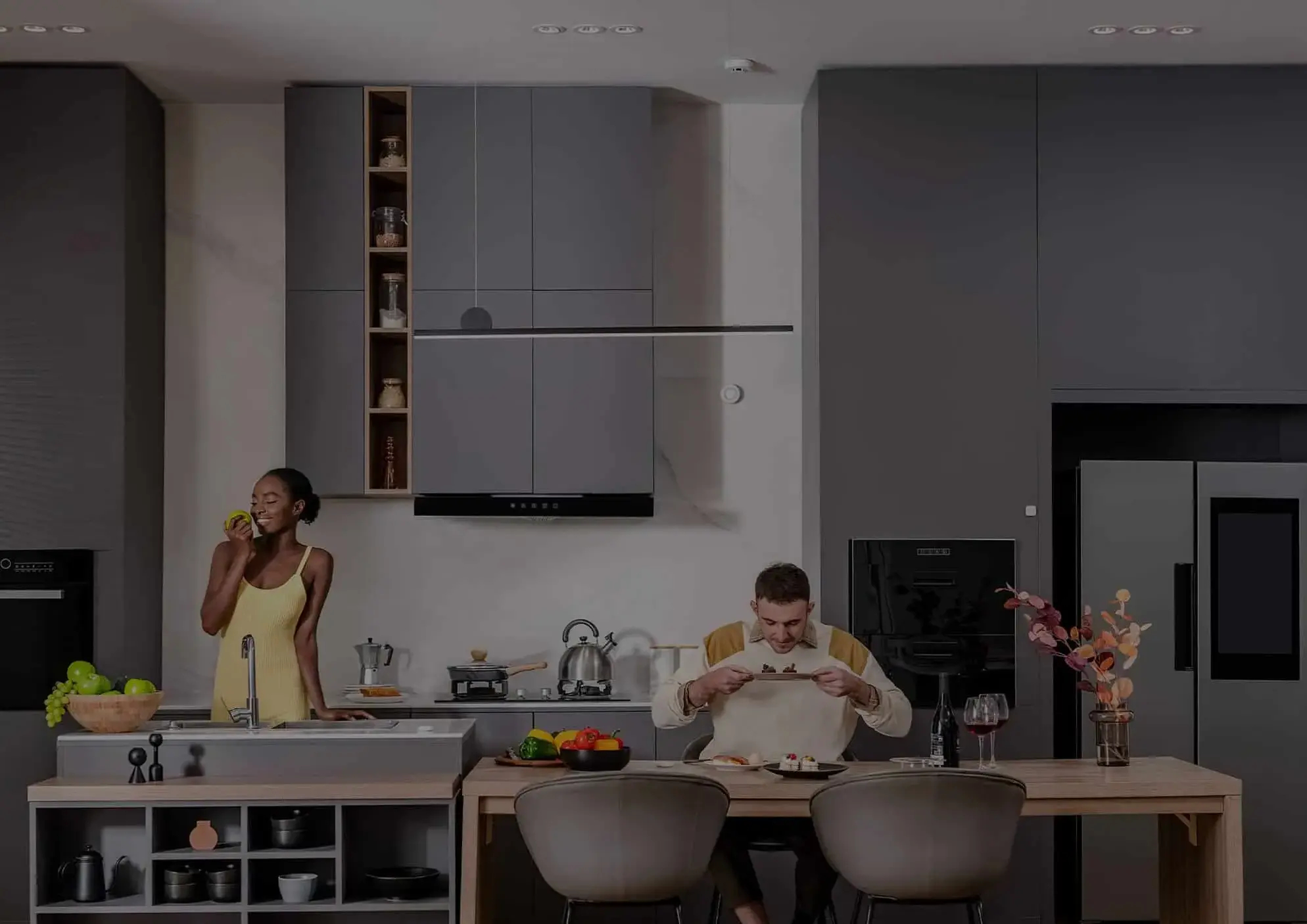Nowoczesna scena kuchenna. Kobieta je jabłko, mężczyzna patrzy na jedzenie. Szare i drewniane odcienie.