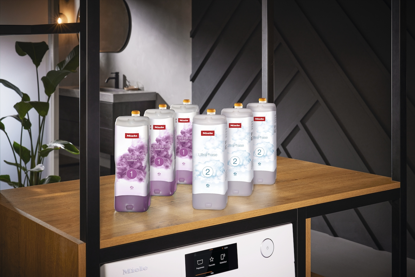 Sieben Waschmittelflaschen auf einem Regal. Einige haben lila Blumendesigns, andere ein blaues Wolkendesign. Darunter eine Waschmaschine.