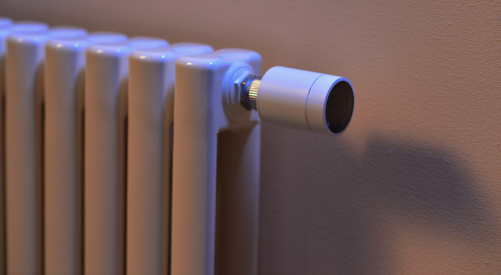 Grzejnik z białym korpusem i inteligentnym termostatem. Termostat jest cylindryczny.