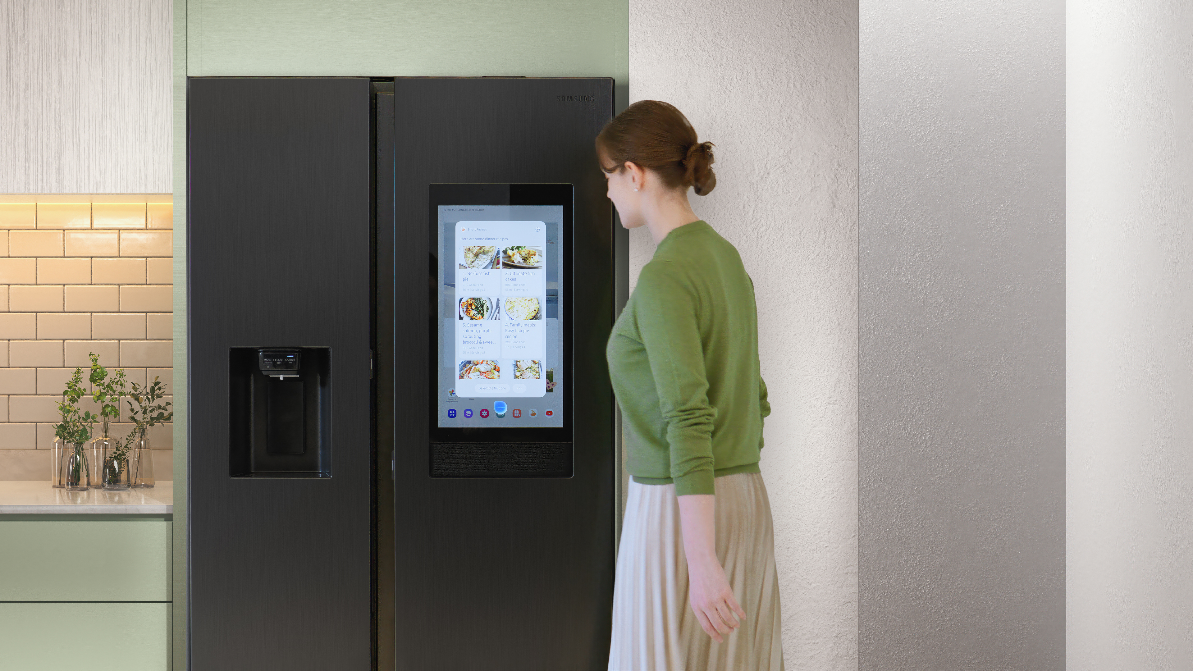 Eine Frau benutzt einen Touchscreen an einem schwarzen Smart-Kühlschrank in einer Küche.