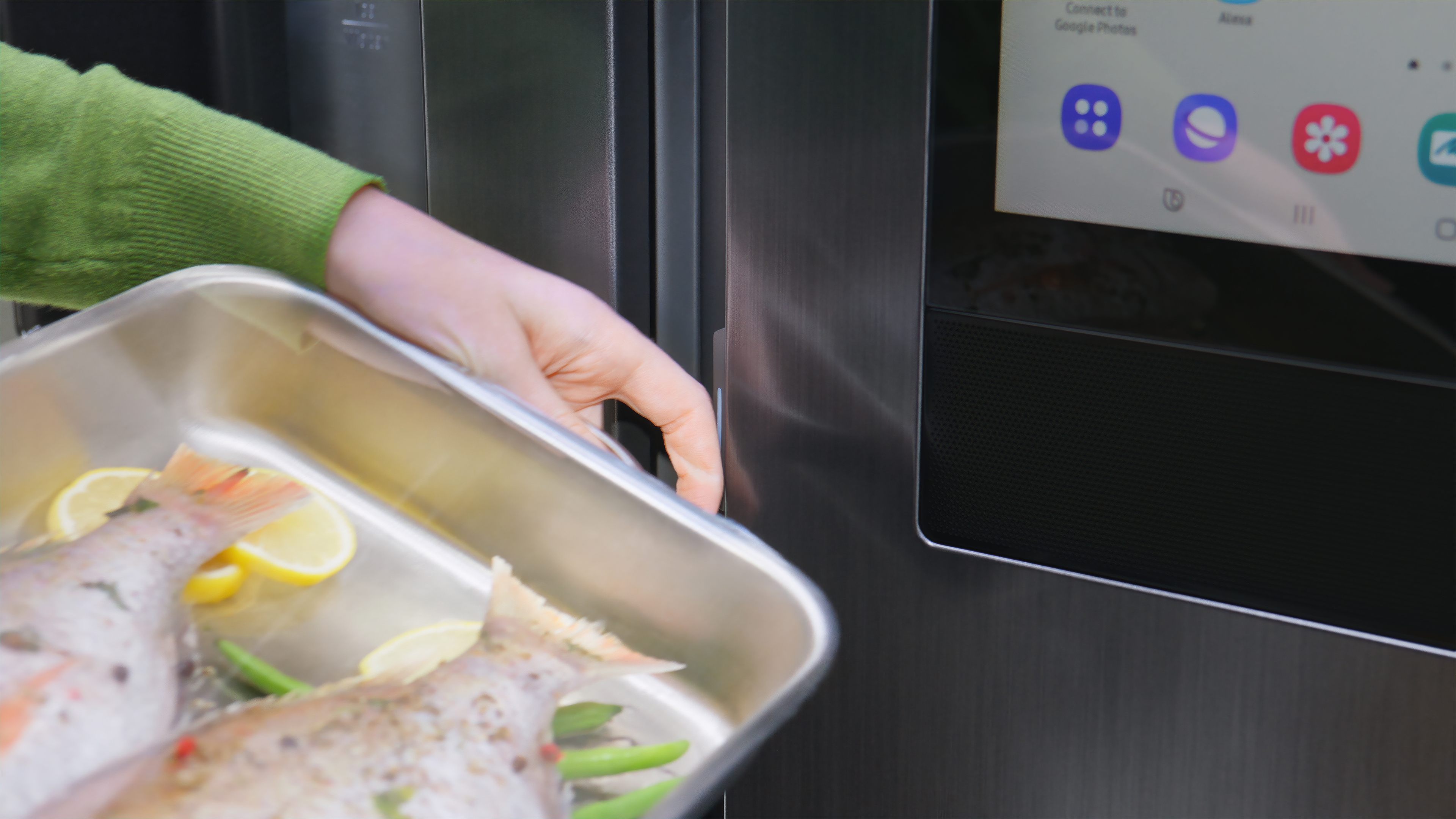 Nahaufnahme einer Hand, die ein Tablett mit Fisch in den Kühlschrank stellt. Das Tablett enthält Zitronen und Kräuter.