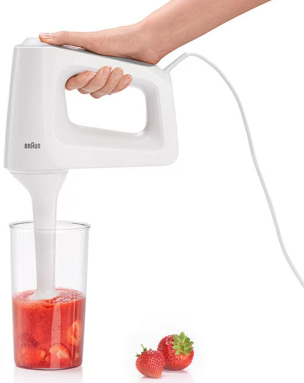 Blender ręczny miksujący truskawki w szklance, z pobliskimi świeżymi truskawkami.