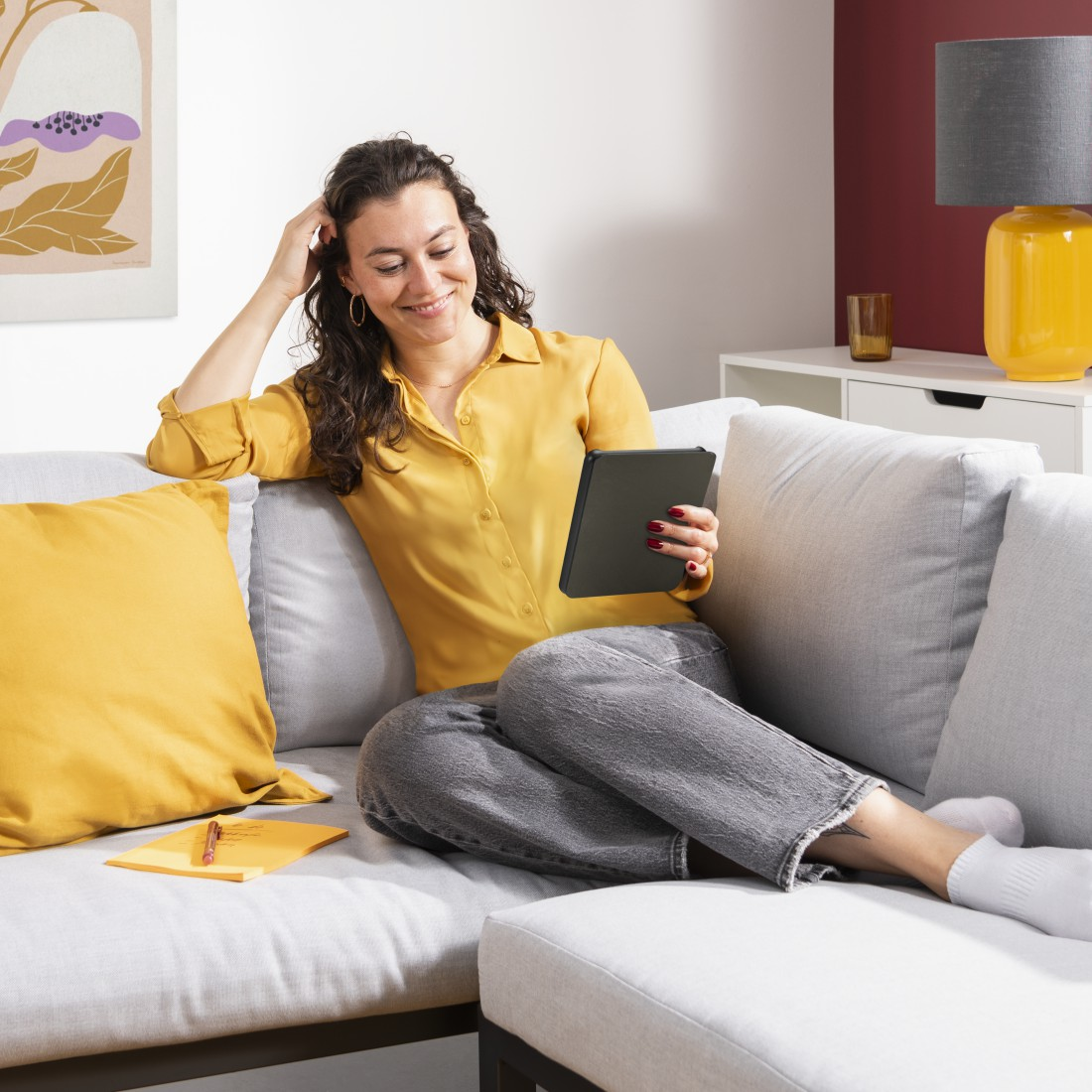 Frau auf dem Sofa mit Tablet, lächelnd.