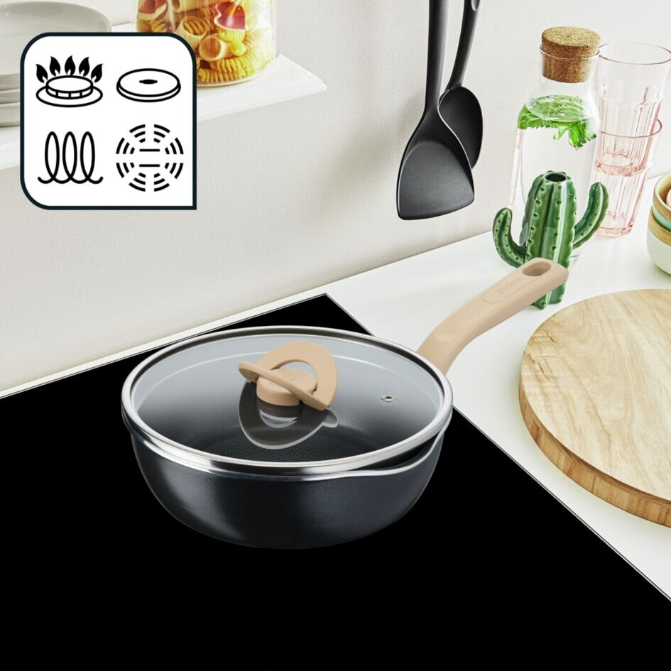 Czarny garnek z pokrywką na płycie grzejnej z ikonami gotowania. Tło obejmuje białą półkę i szkło.