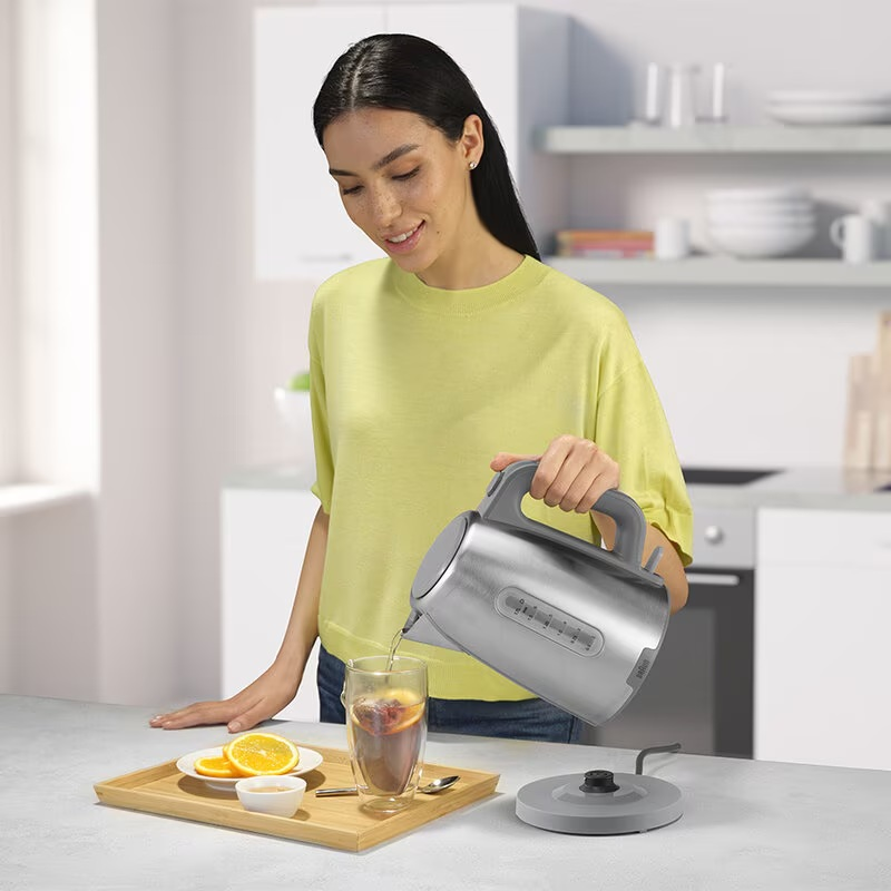 Kobieta nalewa wodę ze stalowego czajnika do szklanki z herbatą i pomarańczami.