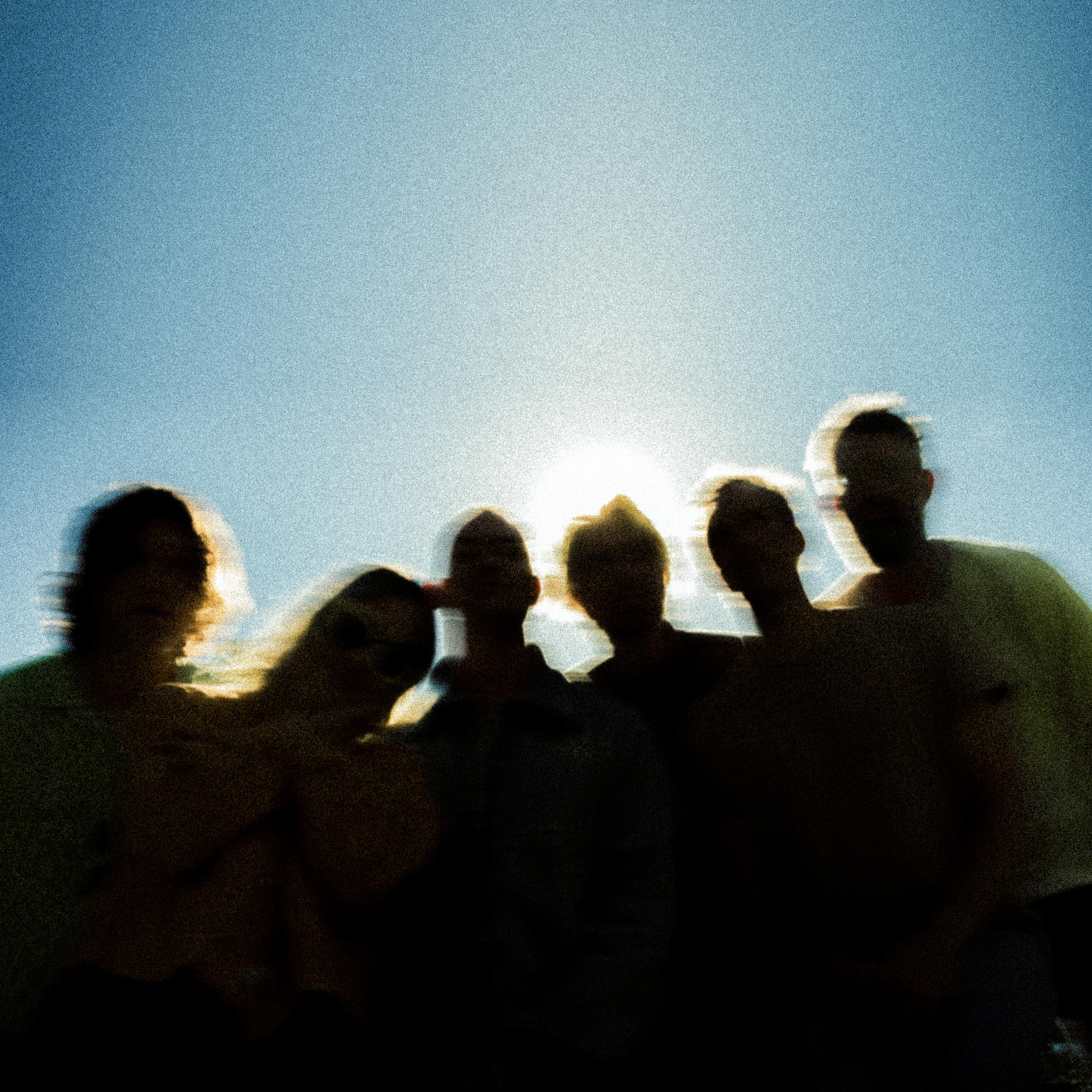Verschwommene Silhouetten von Menschen vor einem hellen, sonnigen Himmel.